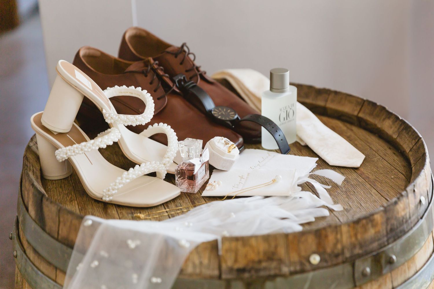 White high heel wedding shoes resting on a rustic wooden wine barrel against blurred background.