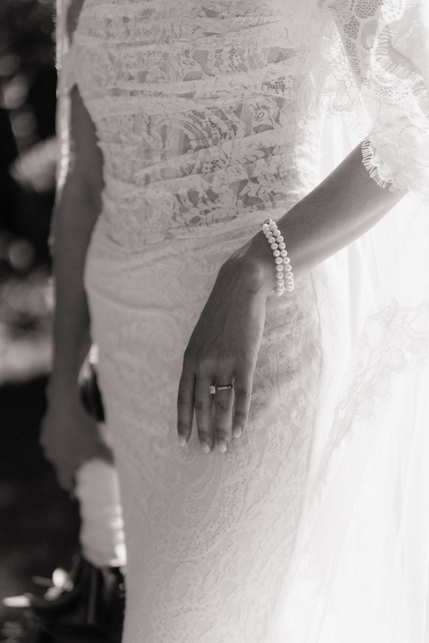 Black and white photo of bride in lace wedding dress wearing pearl bracelet and diamond engagement ring.