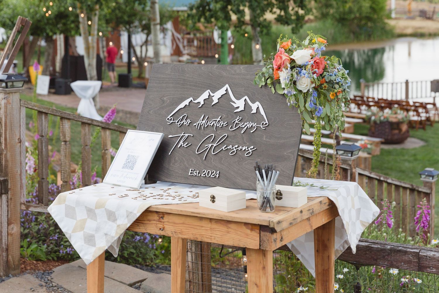 A rustic wooden table displays a mountain-themed wedding welcome sign with wildflower decorations.