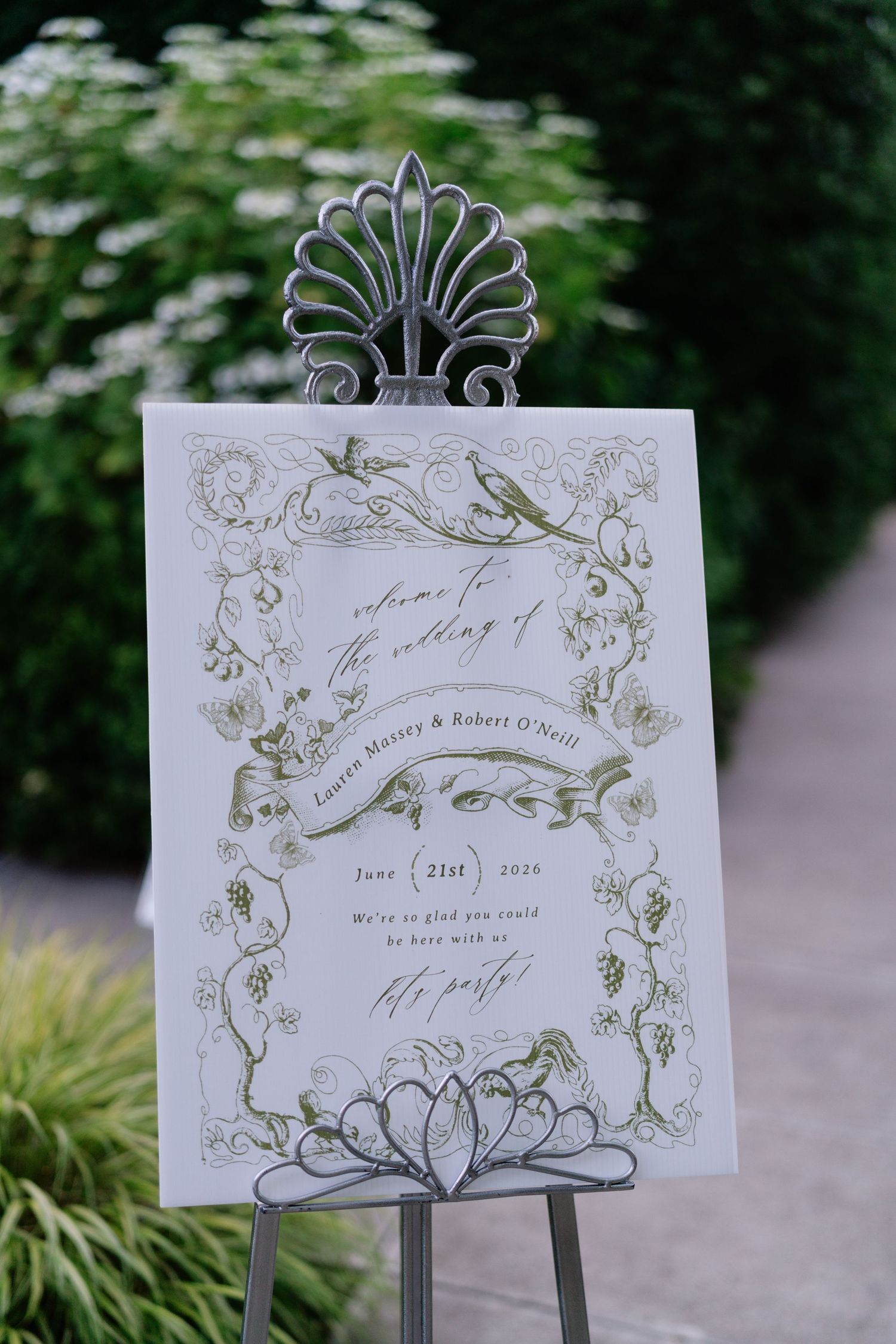 Elegant wedding welcome sign on a decorative easel, featuring floral botanical illustrations and calligraphy script outdoors.