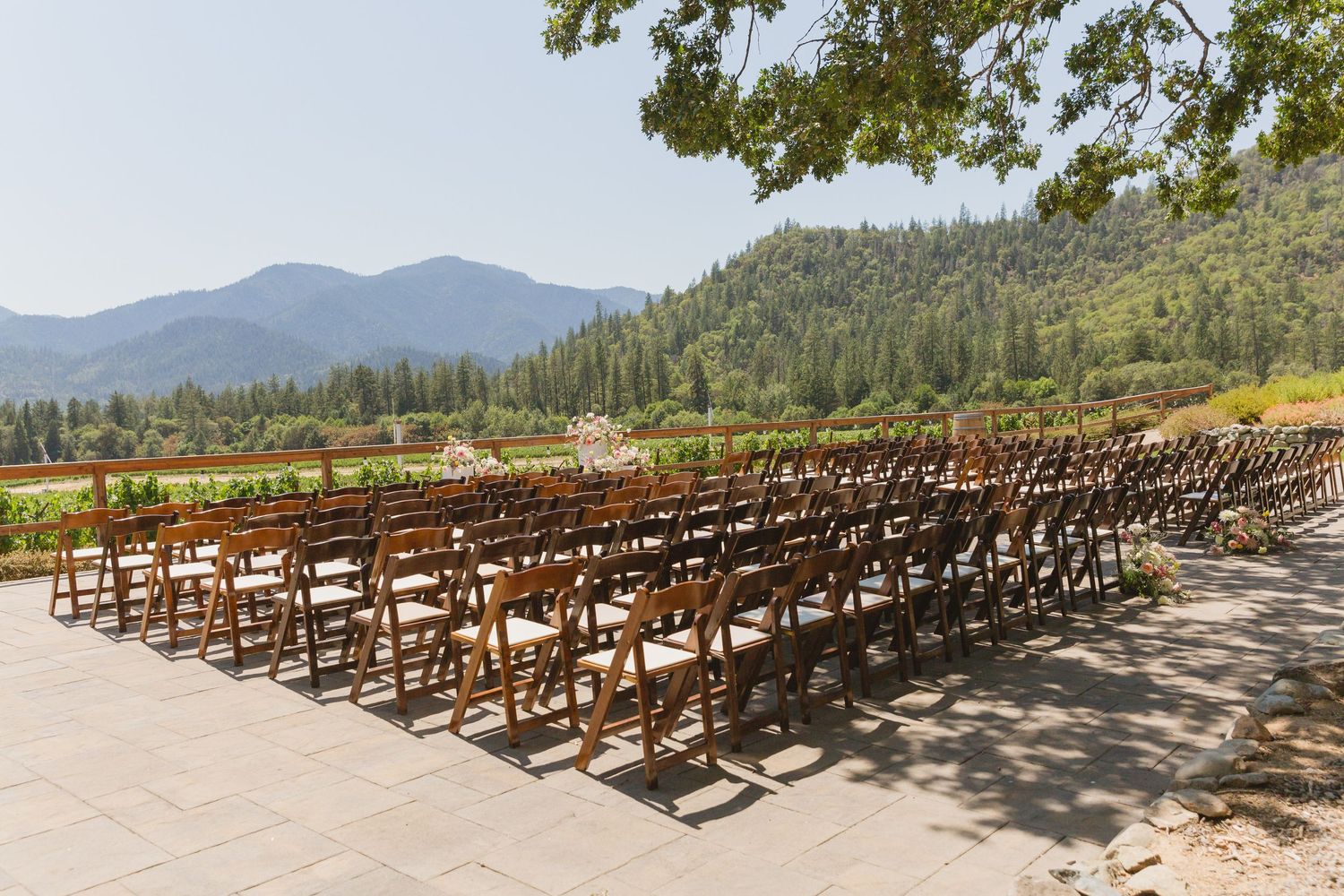 Rows of empty wooden folding chairs set up for an outdoor wedding ceremony against a mountain landscape backdrop.