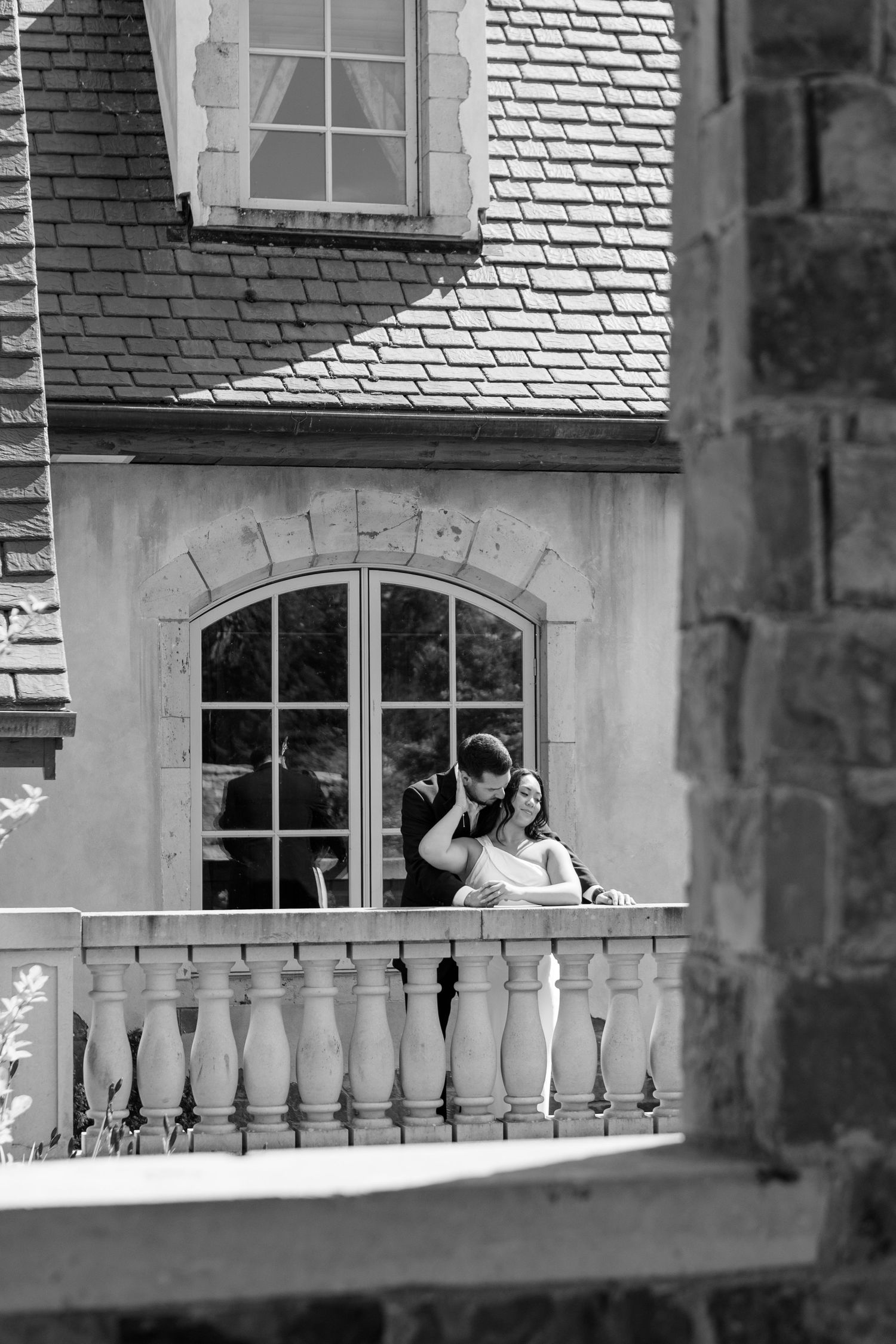 Historic stone balcony with white spindles against gray stone building facade featuring arched windows.