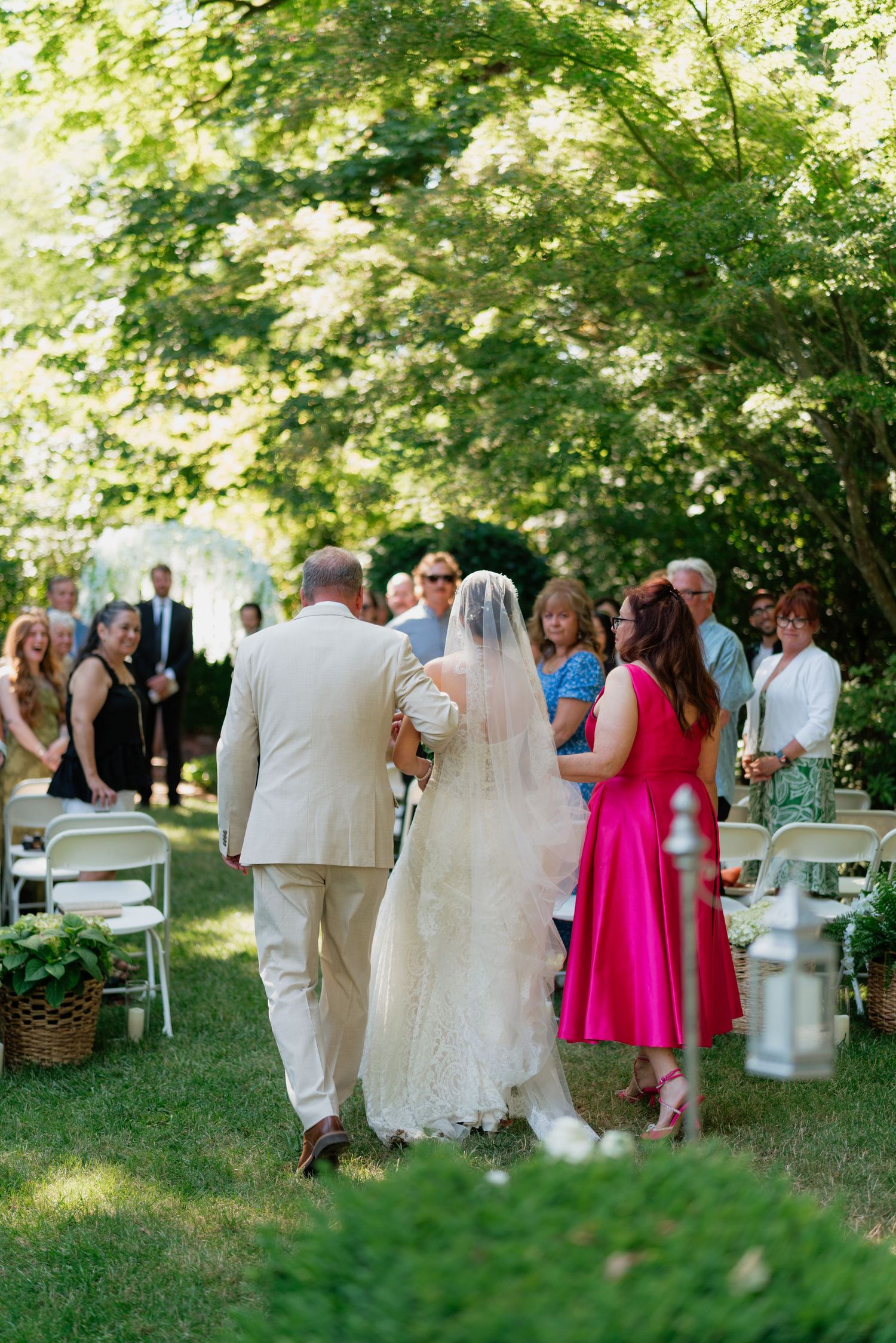 Bride walks down outdoor aisle with escort at garden wedding ceremony.