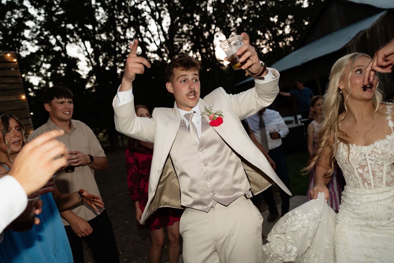 Joyful groom in white suit celebrates with bride at outdoor wedding reception dance party at night.