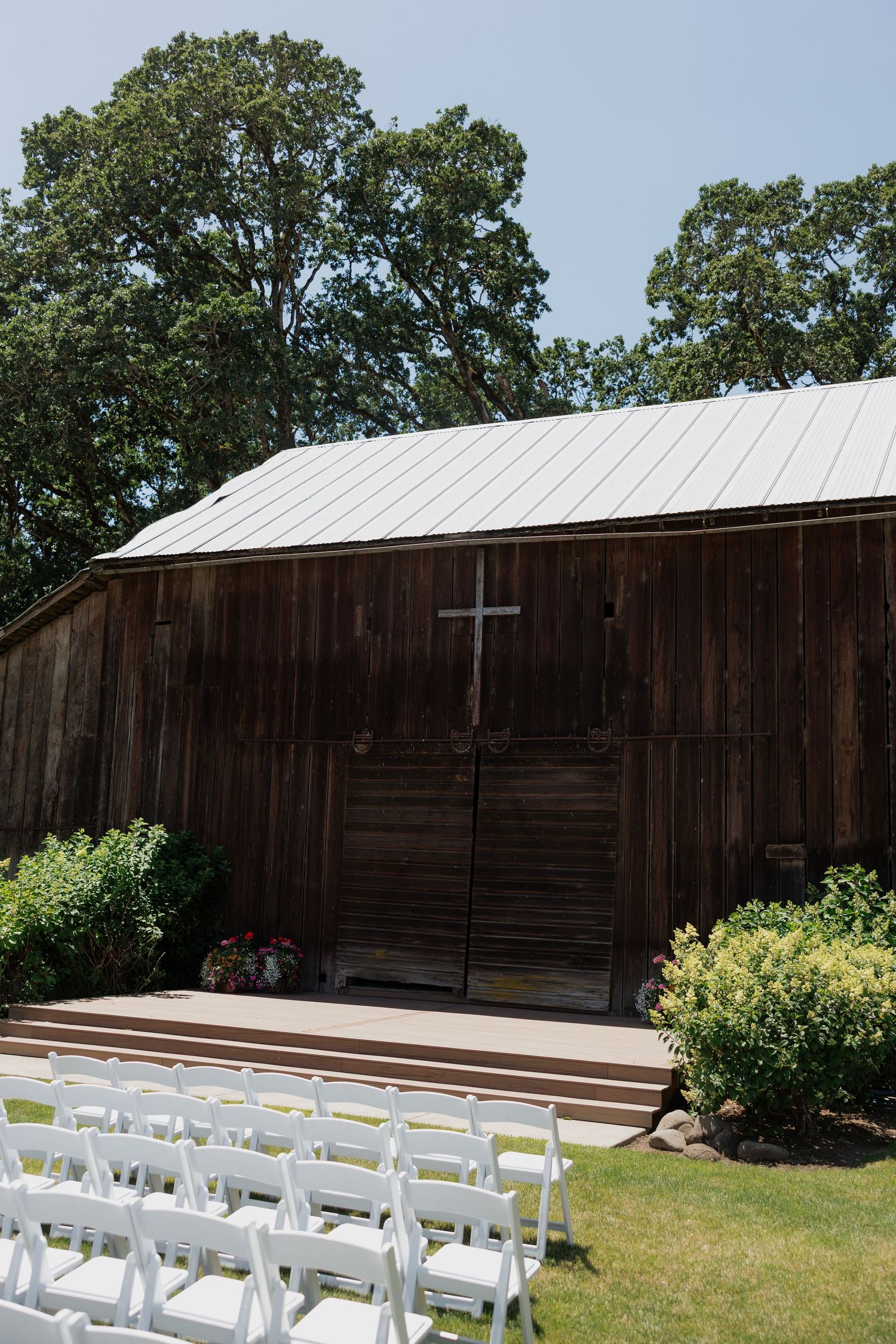 Rustic wooden barn wedding venue with white folding chairs arranged outdoors under blue sky.