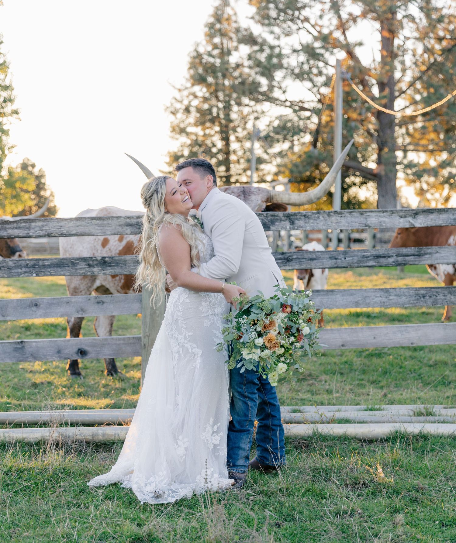 Two people share an intimate moment outdoors during a rustic photo session at sunset with wooden fencing in the background.
