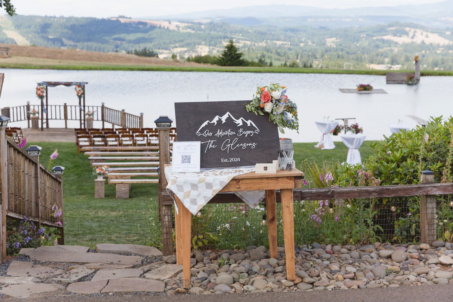 Rustic wooden wedding reception layout featuring tables and benches overlooking a mountain landscape.