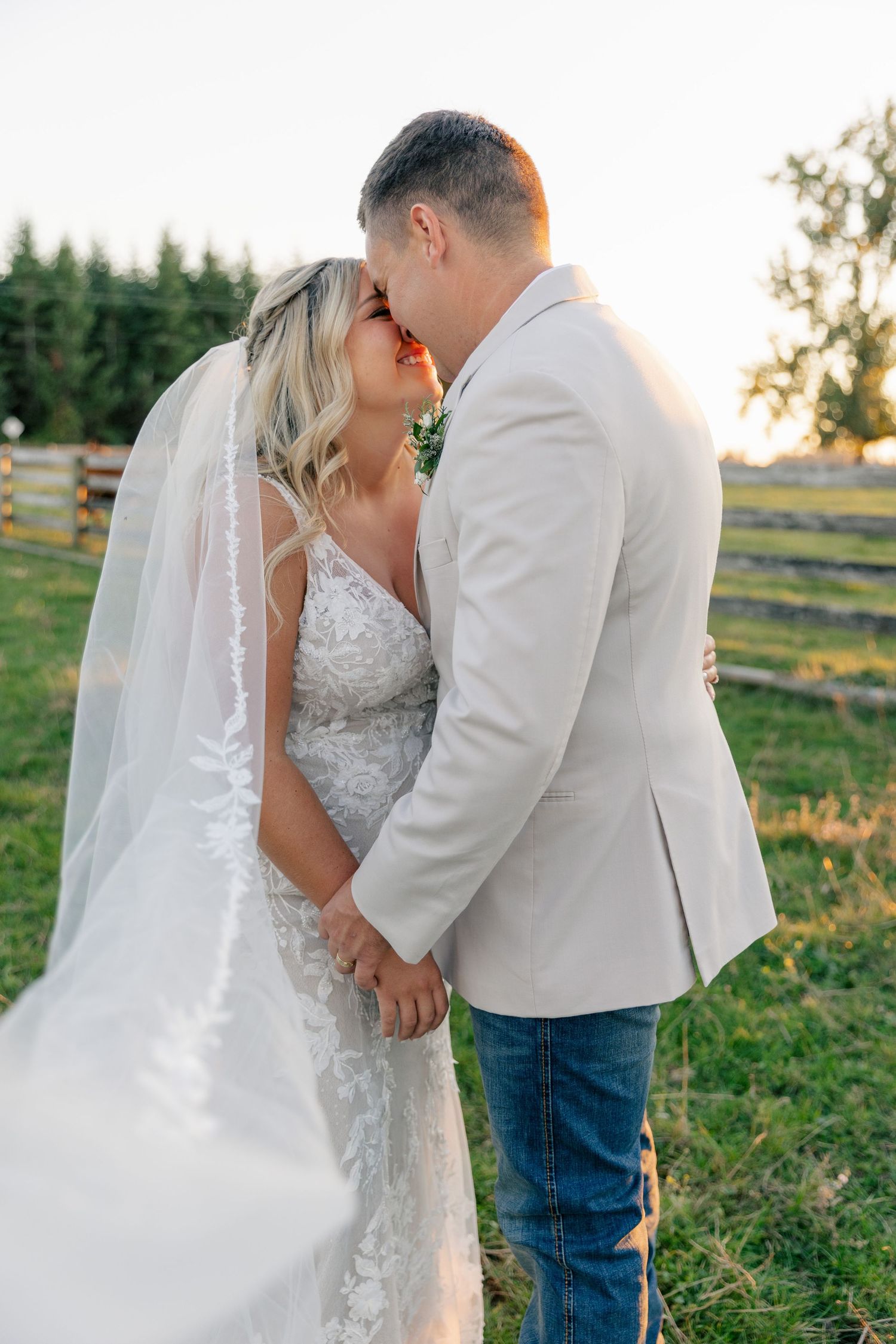 A romantic sunset photo shows a bride in white lace dress and groom in light attire sharing tender moments in a field.