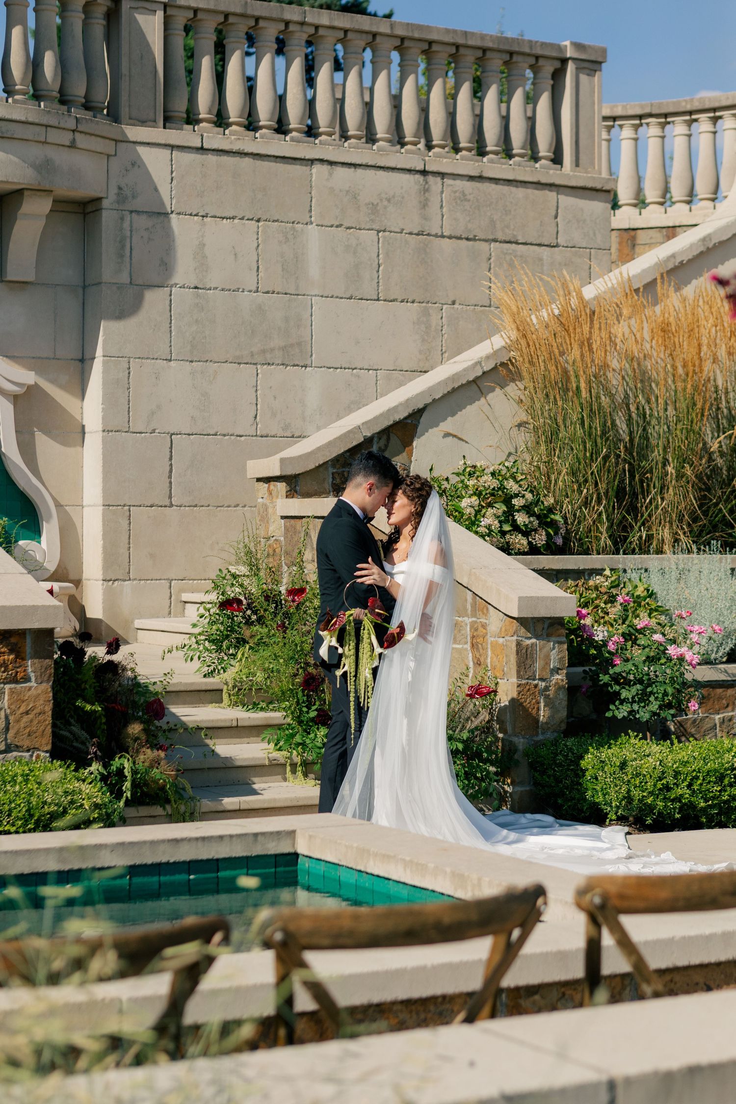 Romantic couple shares an intimate moment on grand stone stairs surrounded by lush garden and architecture.