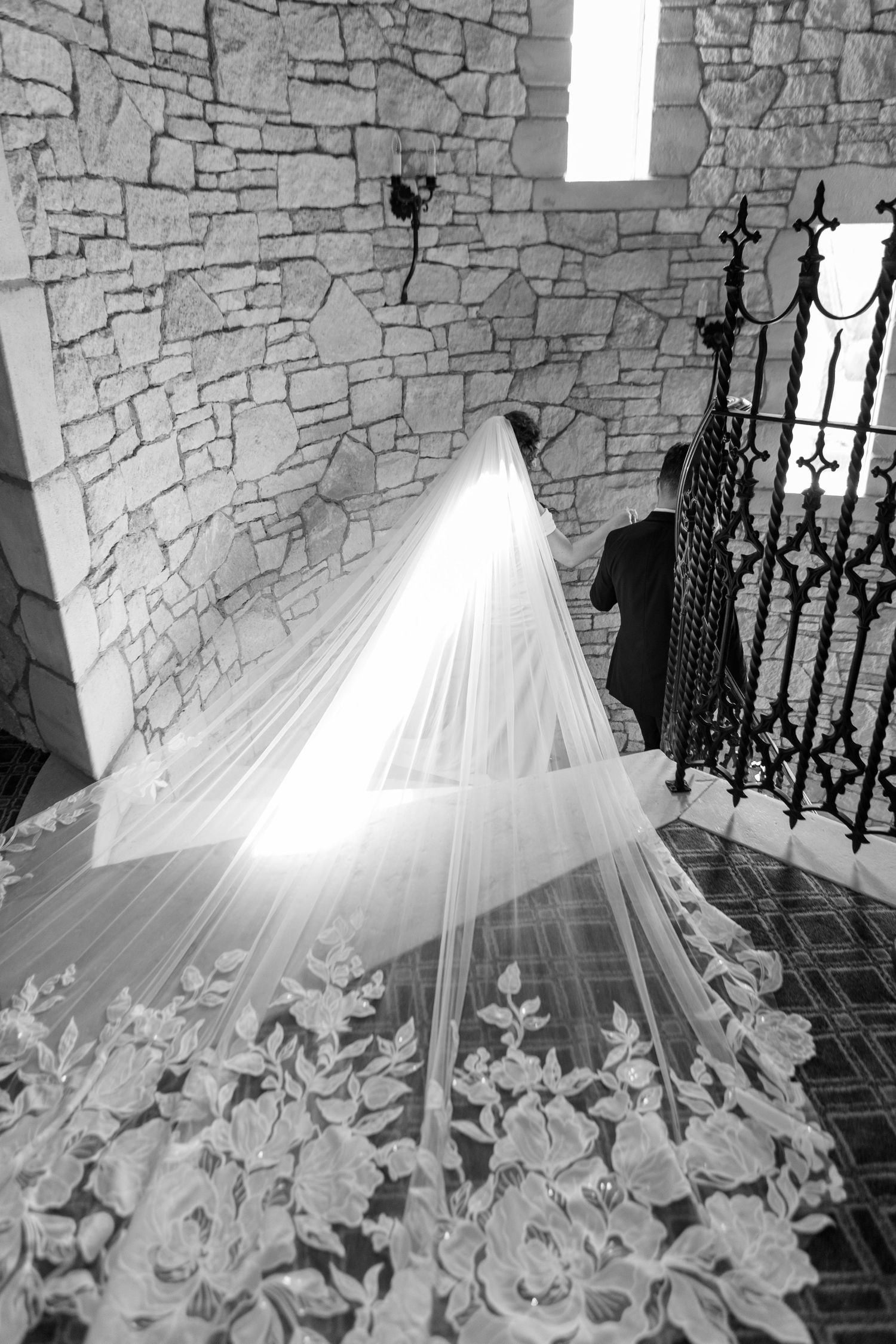 A flowing white wedding dress train with intricate details displayed on stone steps with natural lighting.