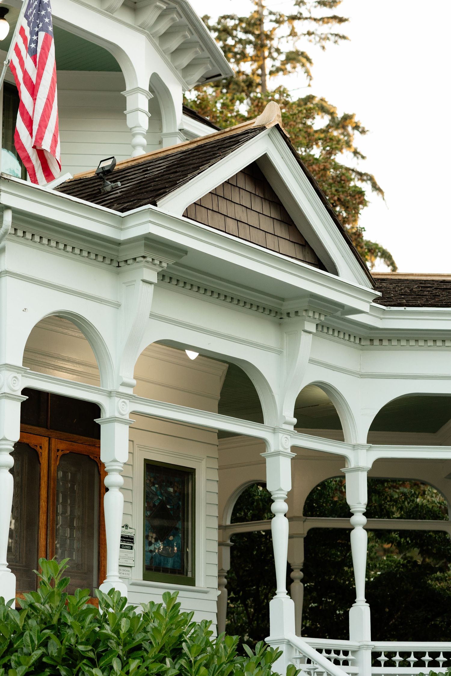 White Victorian house with arched porch columns and American flag, showcasing classic American architectural details.