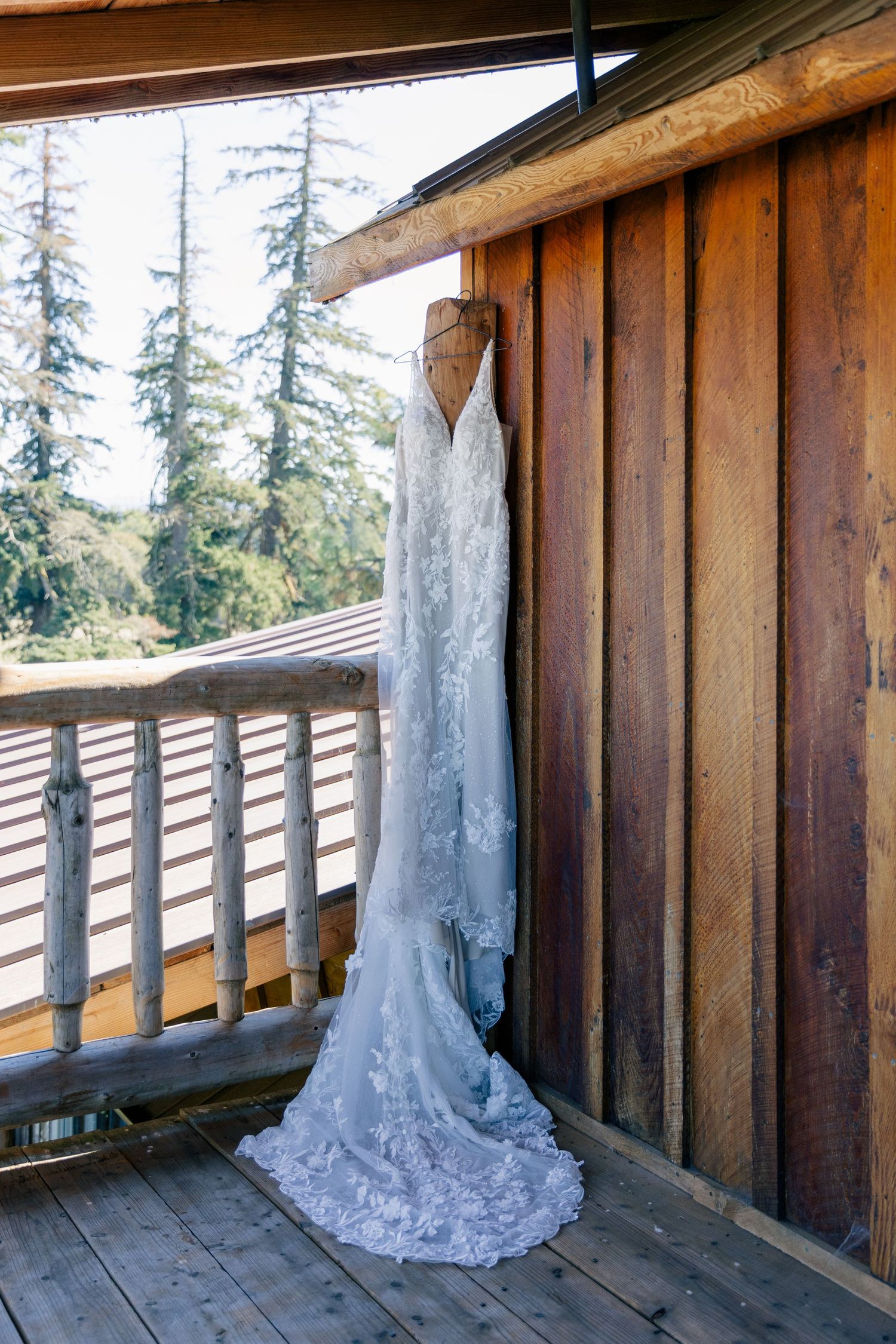 A white wedding dress train displayed along a wooden deck railing with evergreen trees in the background.