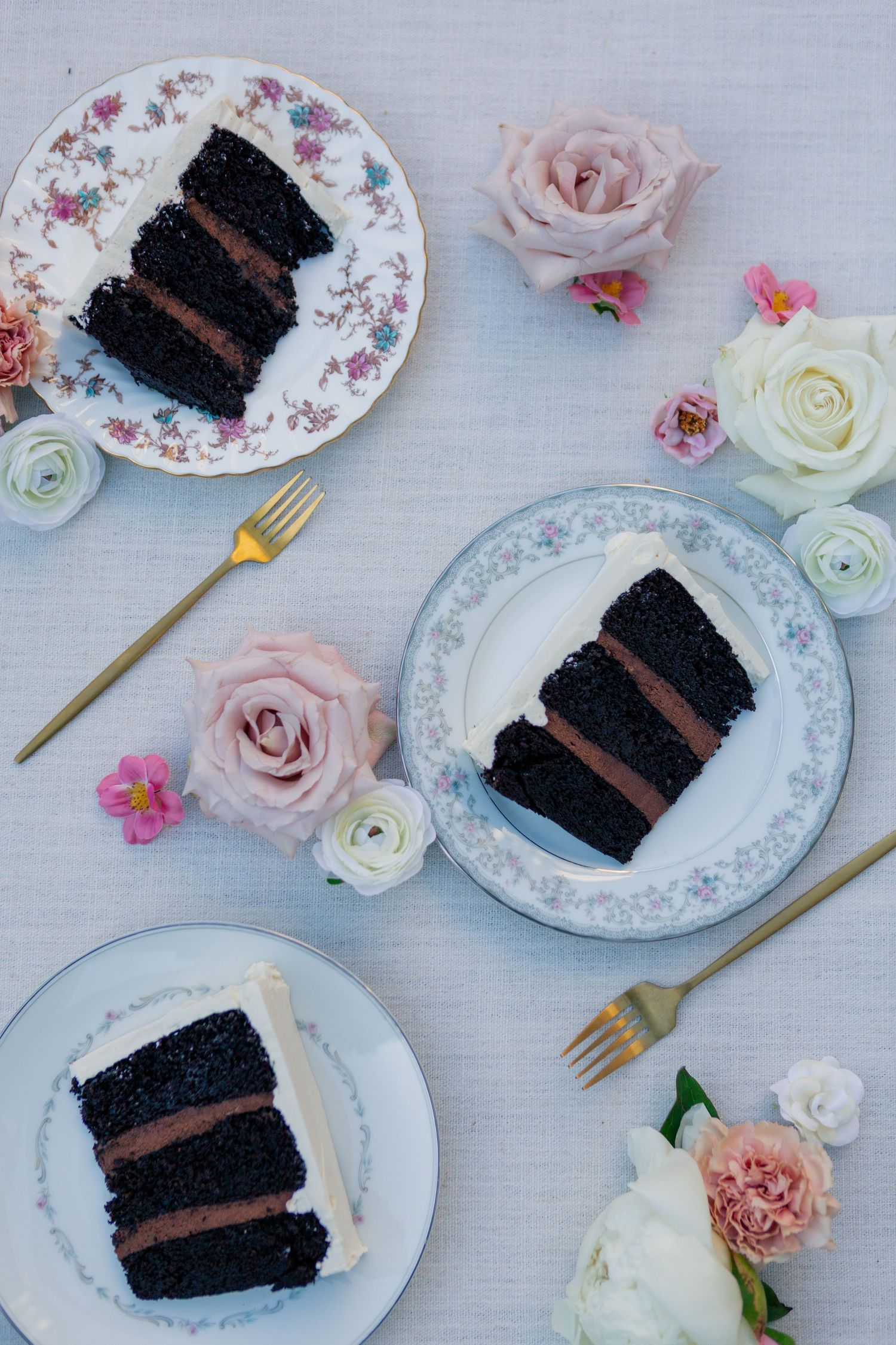 Slices of rich chocolate layer cake served on floral china plates with pink and white roses and gold forks.
