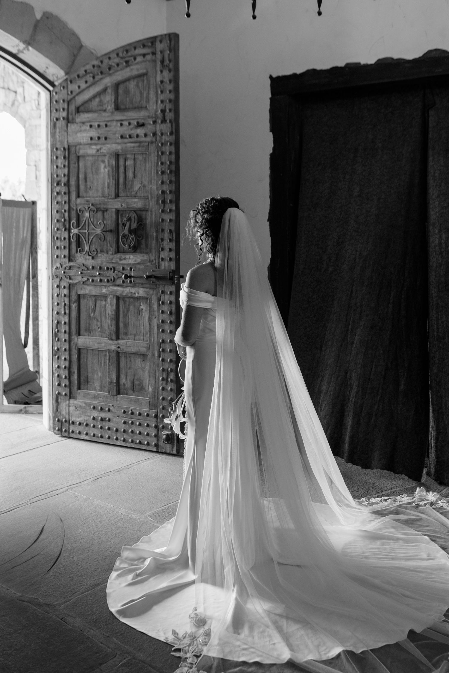 A series of black and white photos shows a flowing wedding dress with cathedral veil in a rustic interior setting.