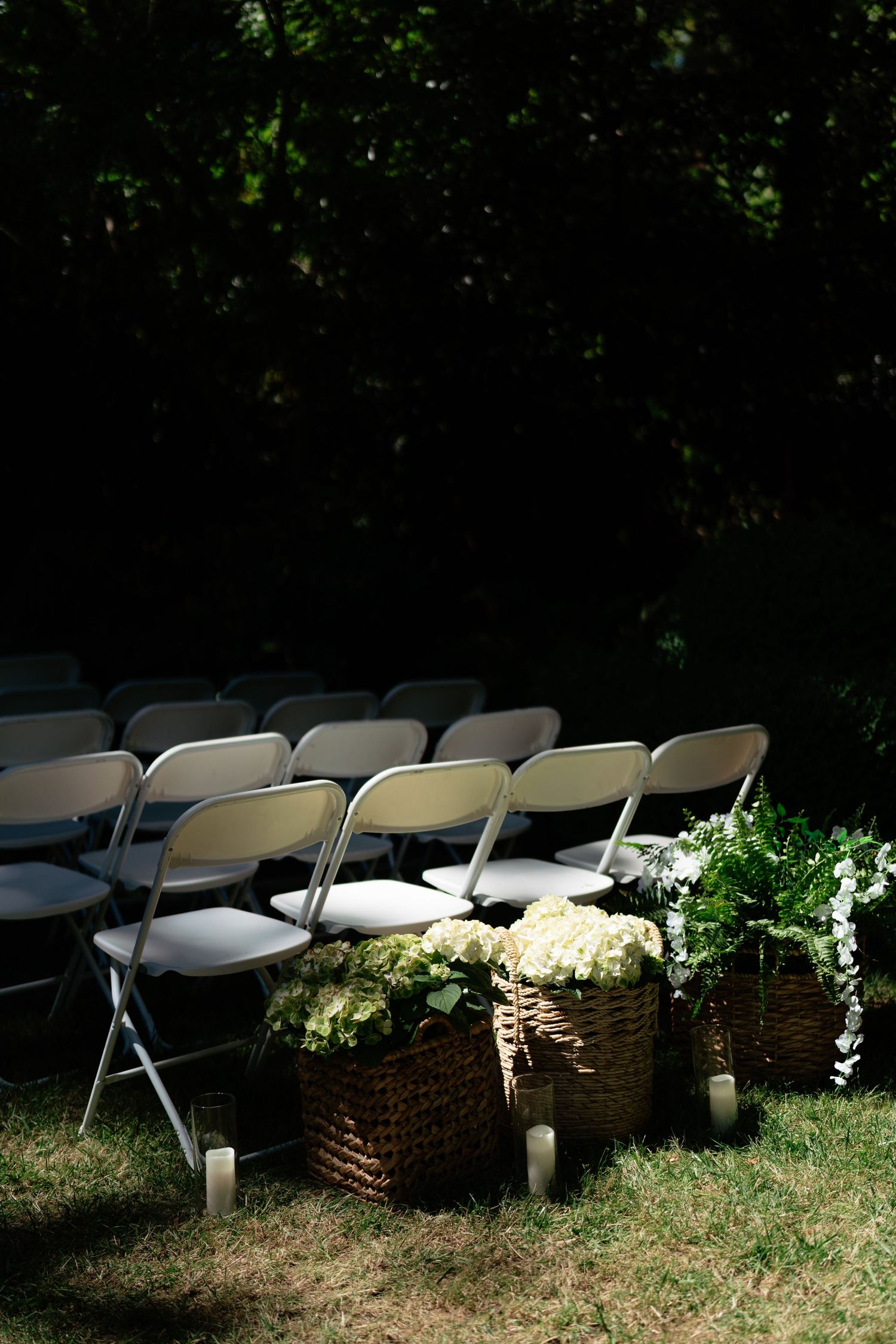 Rows of gray folding chairs set up outdoors for a wedding ceremony with wicker baskets of white flowers.
