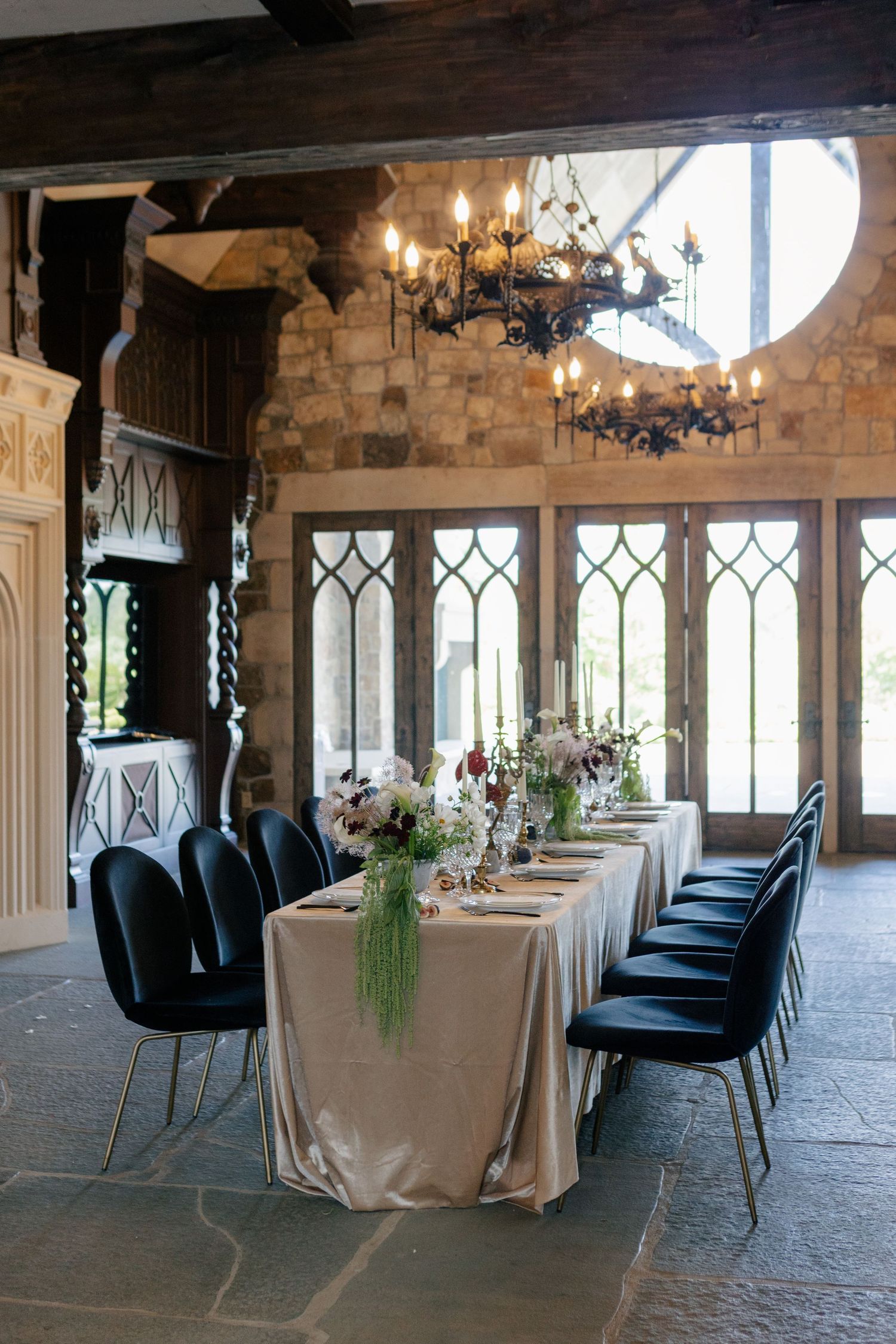 Elegant wedding reception venue with stone walls, Gothic windows, chandeliers and tables set with navy chairs.