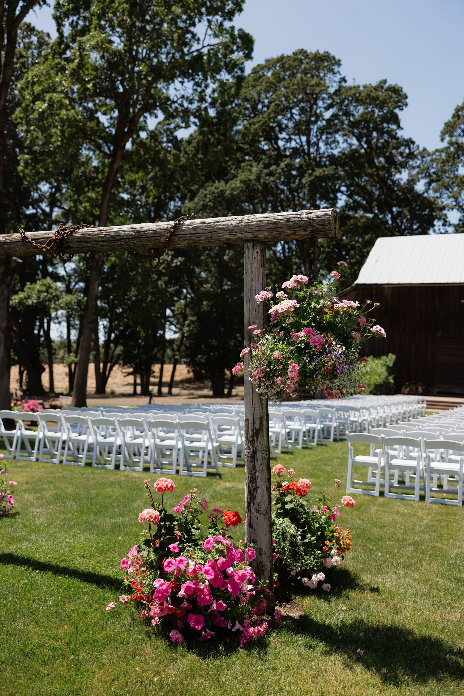 Rustic wooden wedding arch adorned with pink roses beside white chairs set up for an outdoor ceremony.