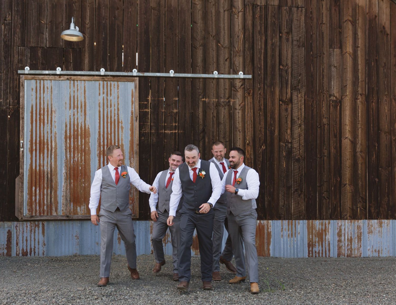 Wedding party posed in front of rustic corrugated metal and wooden barn wall.