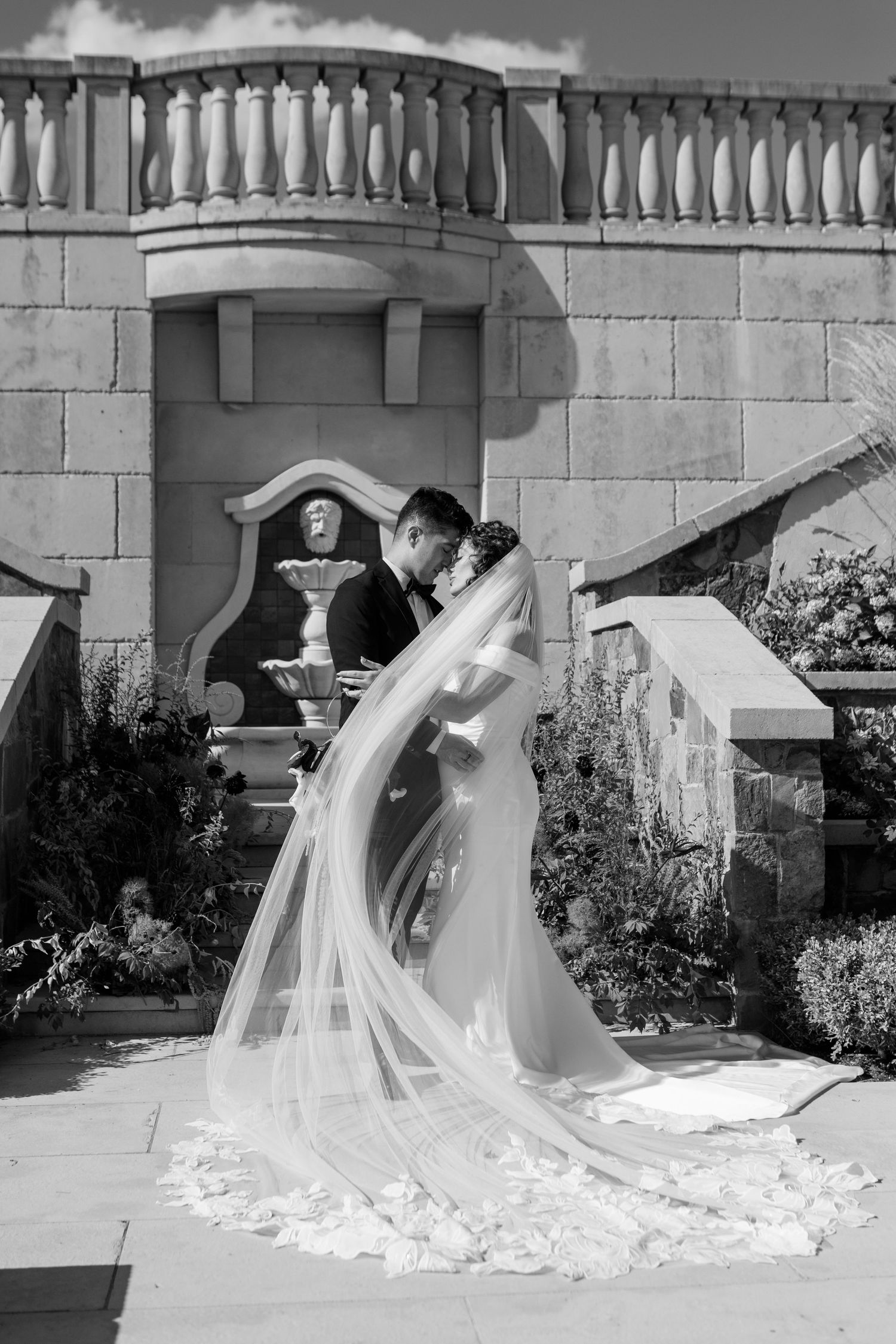 A series of romantic wedding photos showing cascading white veils flowing across a stone courtyard in black and white.