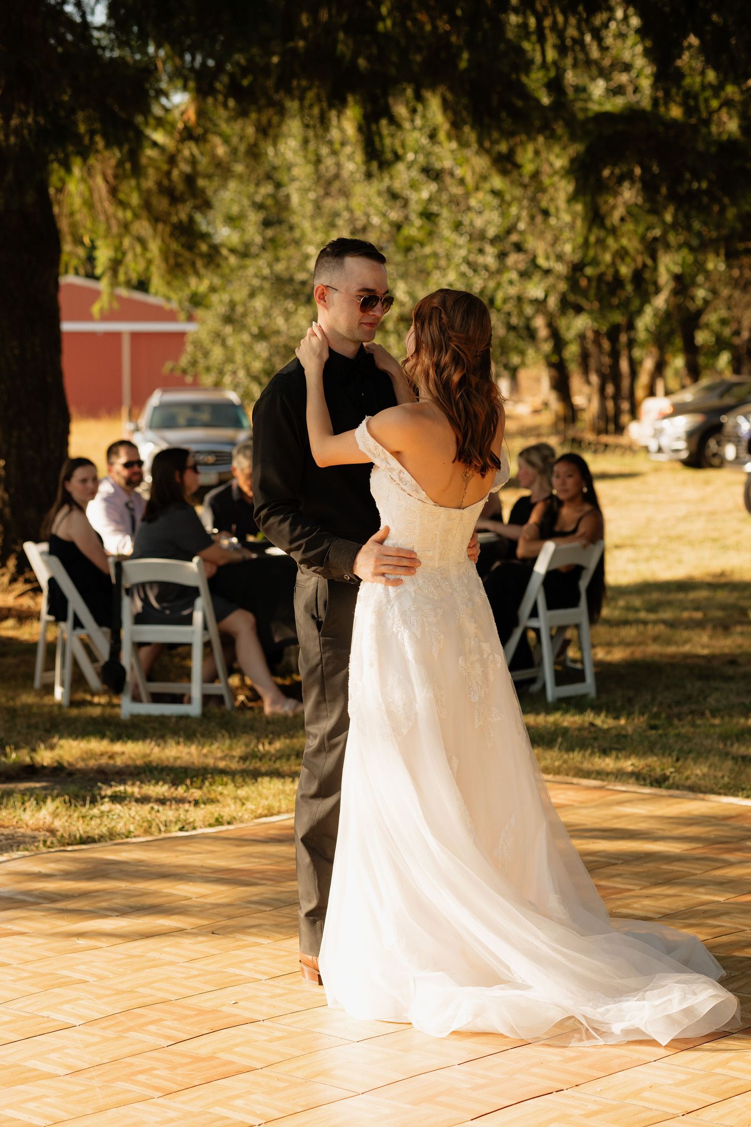 Bride and groom share their first dance outdoors on a wooden floor surrounded by seated wedding guests.