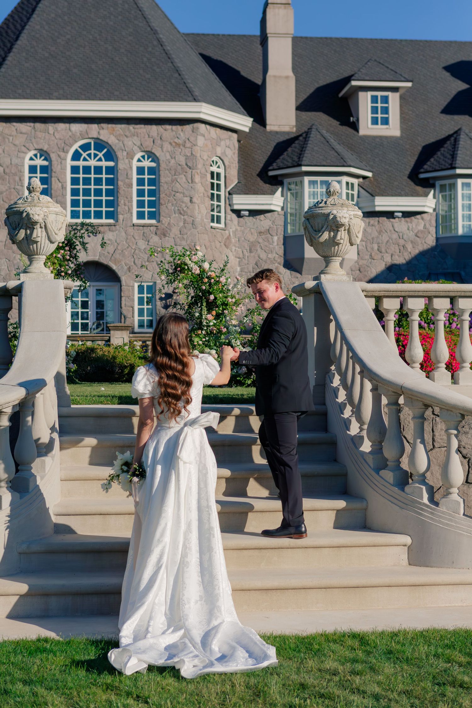 Elegant wedding photos captured on a stone terrace with ornate white architectural columns and balustrades outside a mansion.