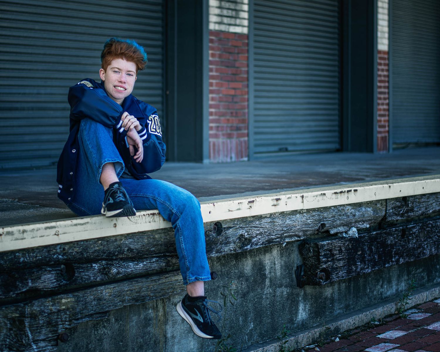 Urban portrait series showing someone sitting on concrete steps against brick buildings in moody lighting.