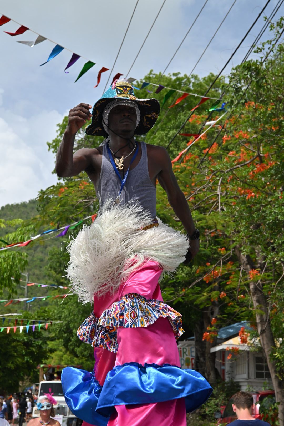 Dancer in vibrant pink and blue costume with white fringe performs at an outdoor festival under colorful bunting.