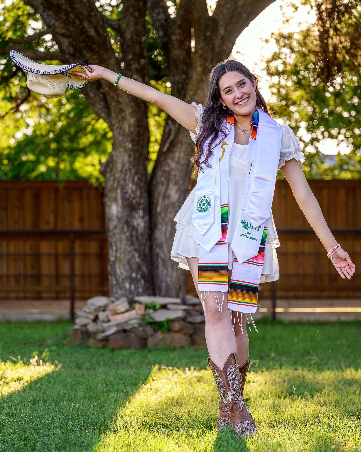 A person in western boots and white attire strikes a playful pose while dancing outdoors in a backyard setting.