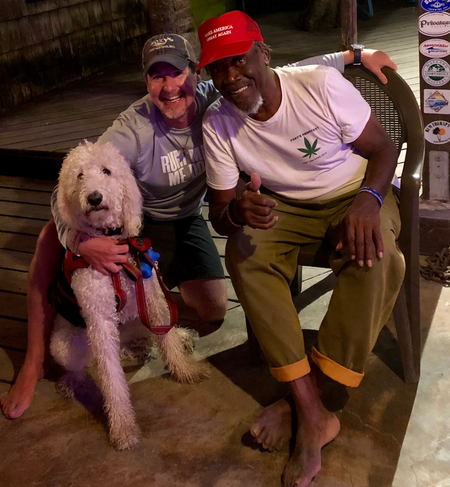 A friendly group sitting together with a fluffy white goldendoodle dog on a wooden deck.