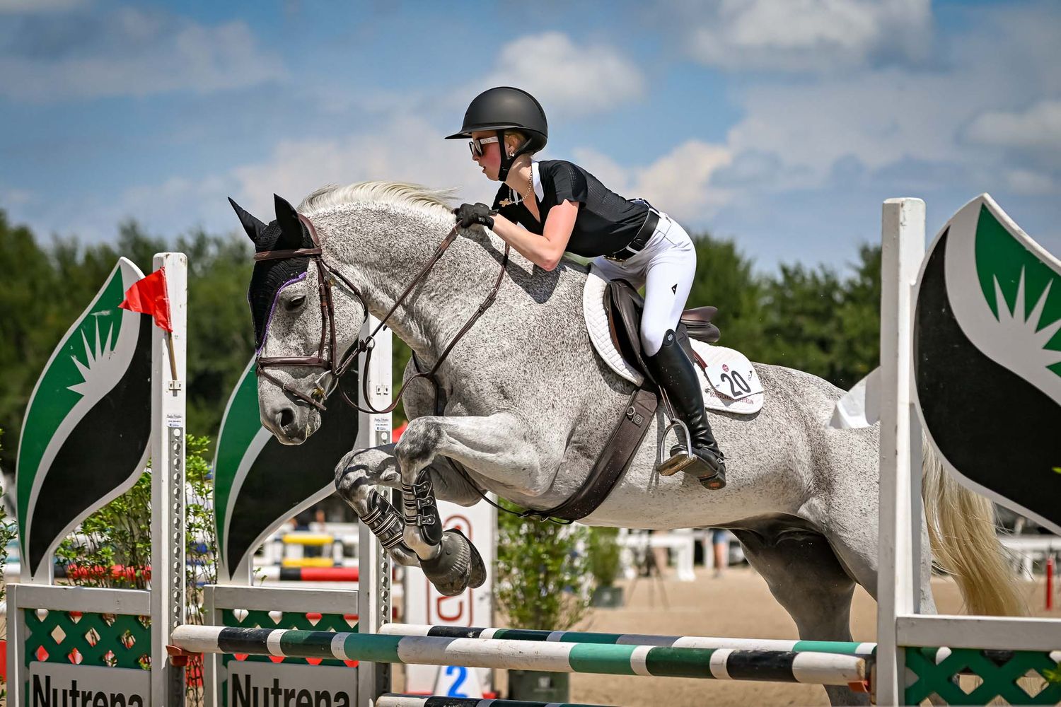 Rider and horse clearing a jump rail during a show jumping competition by professional sport horse photographer Sean Stacey in Texas.