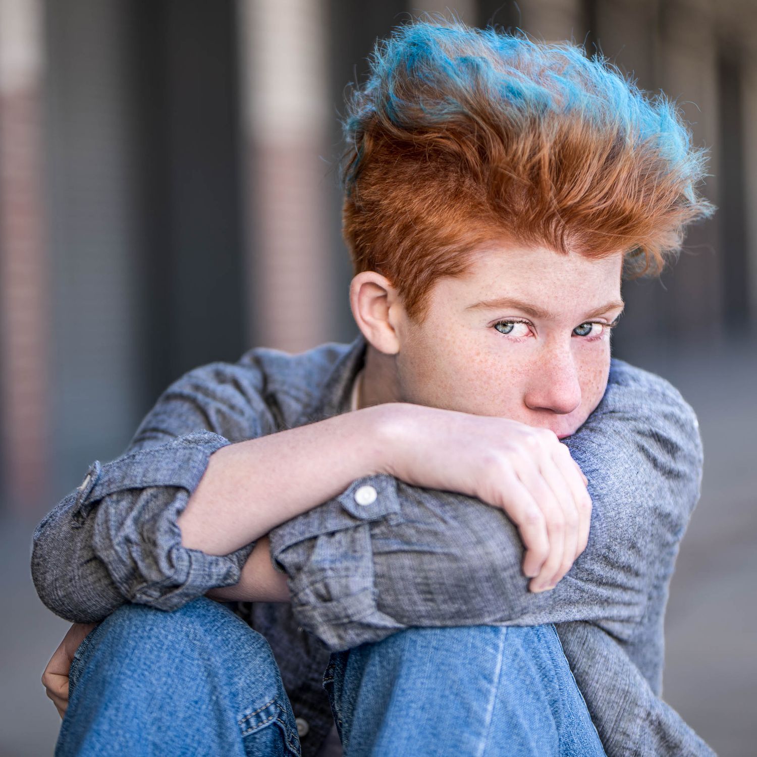Graduating senior with a deep gaze with face hidden behind their sleeve in a grungy area of Ft. Worth during a senior portrait session.