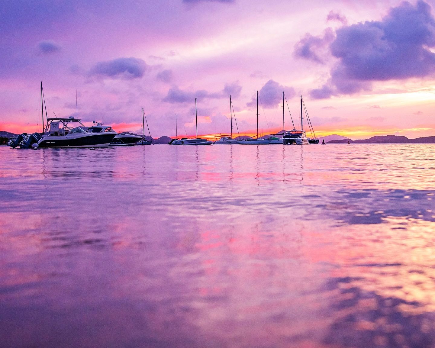 Panoramic sunset view over a calm Cruz Bay, St. John, USVI with boats silhouetted against vibrant purple and pink sky.