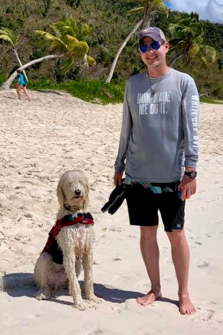 A sandy beach scene with a goldendoodle dog enjoying time by the ocean.