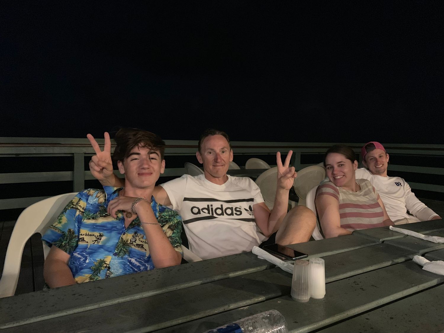 A group of people sitting in stadium bleachers making peace signs and gestures while smiling.