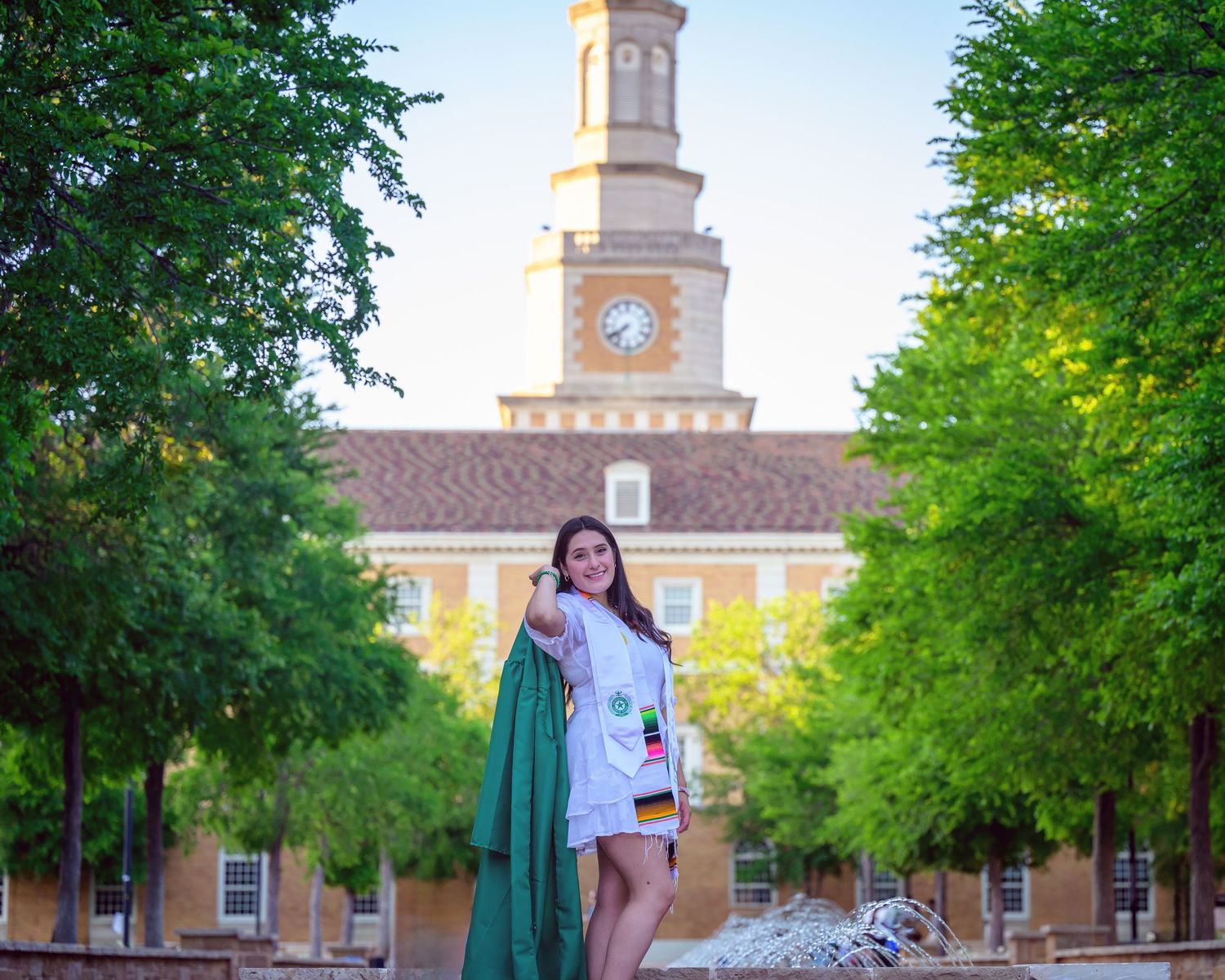 College senior with cap and gown photographed outdoors at UNT for modern editorial-style graduation portraits.