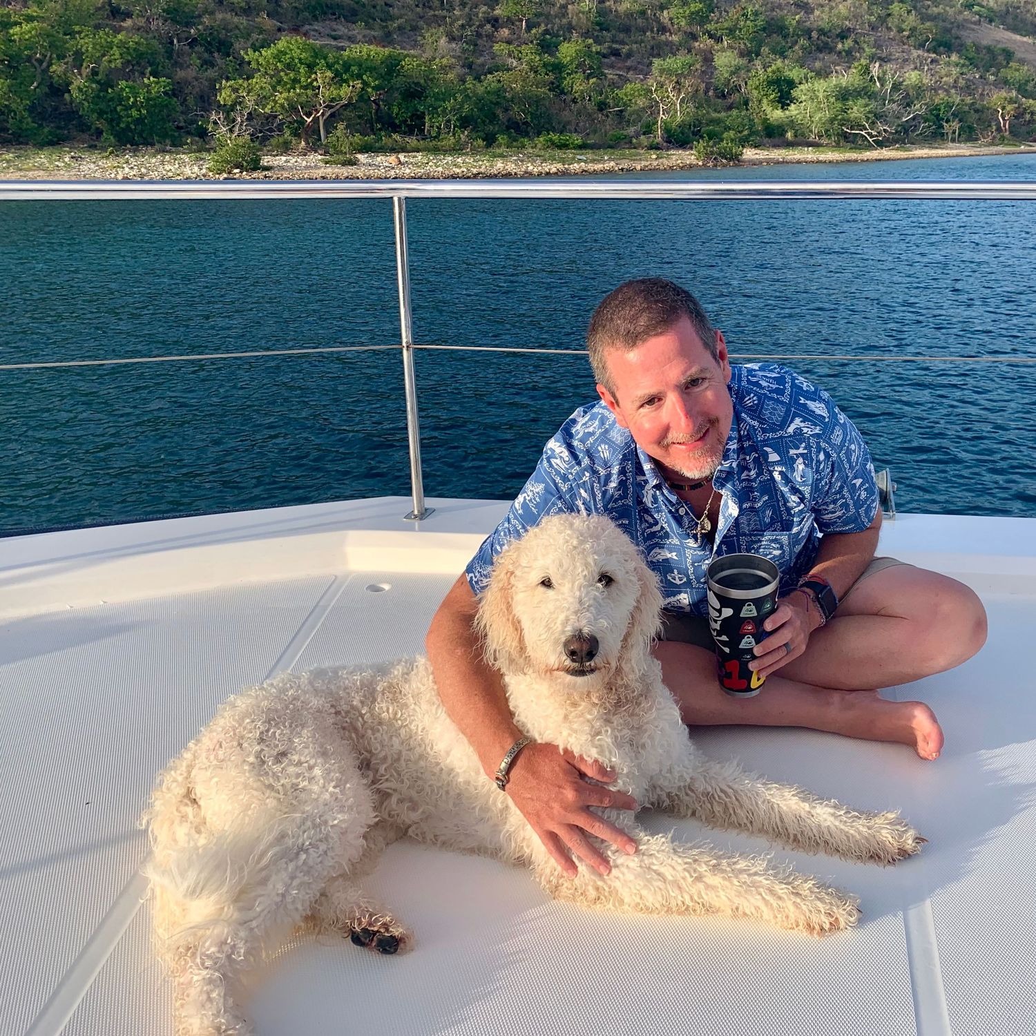 A fluffy white dog relaxing on the deck of a boat with ocean views in the background.