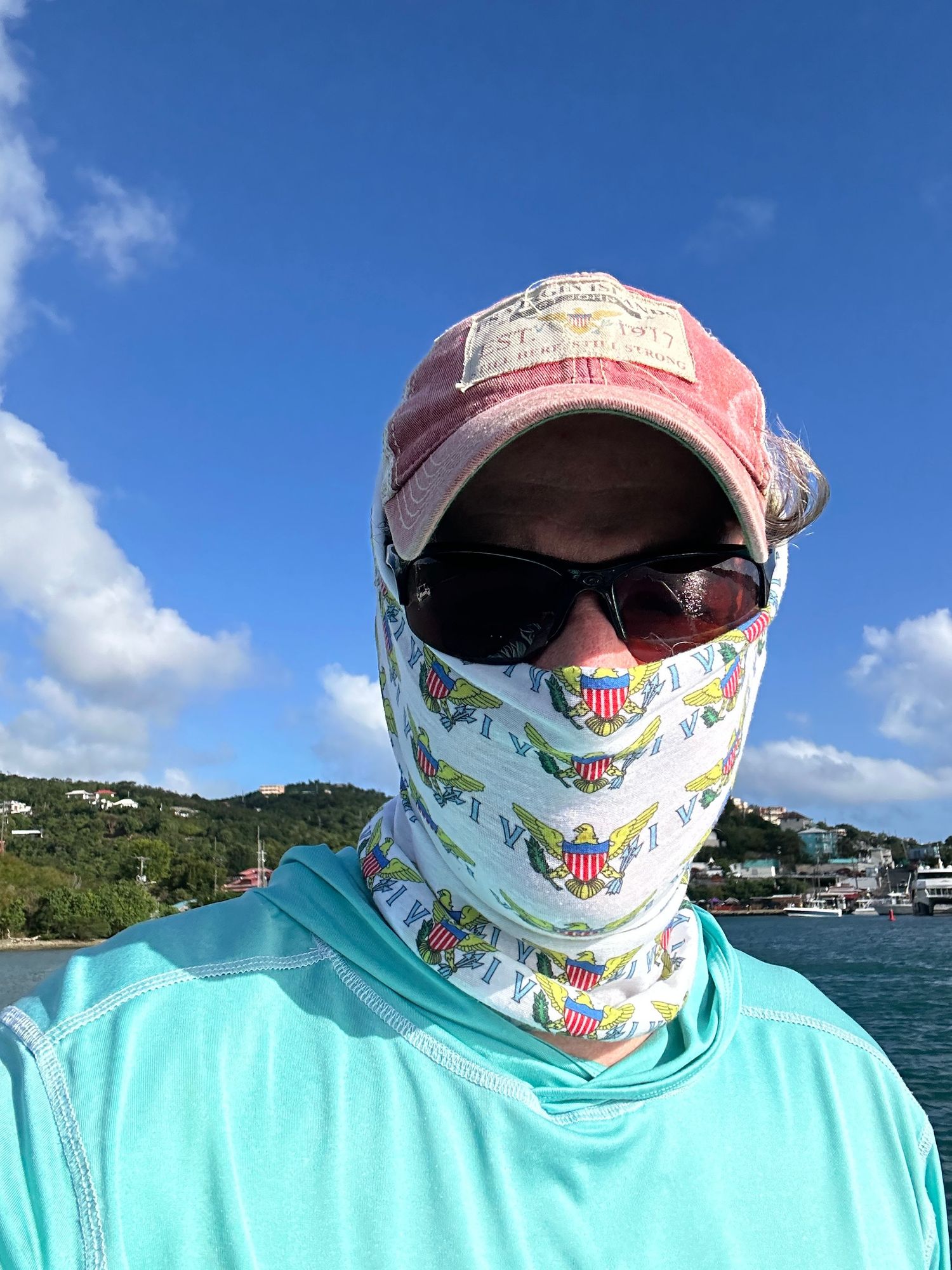 Someone wearing a sun protective face covering, hat, and turquoise shirt while boating on bright blue waters of St. John..