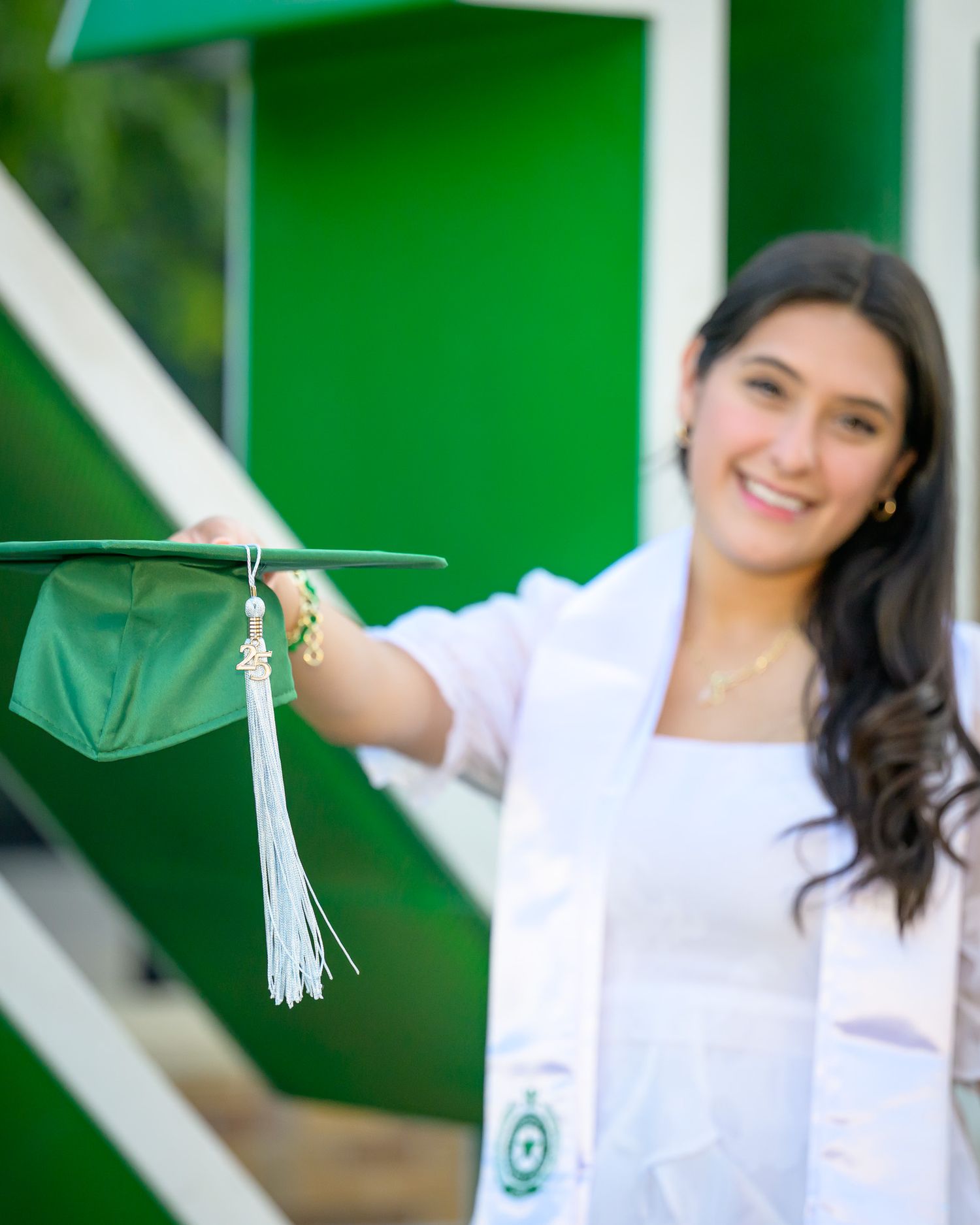 A person in a white top poses against a bright green background with decorative tassels.