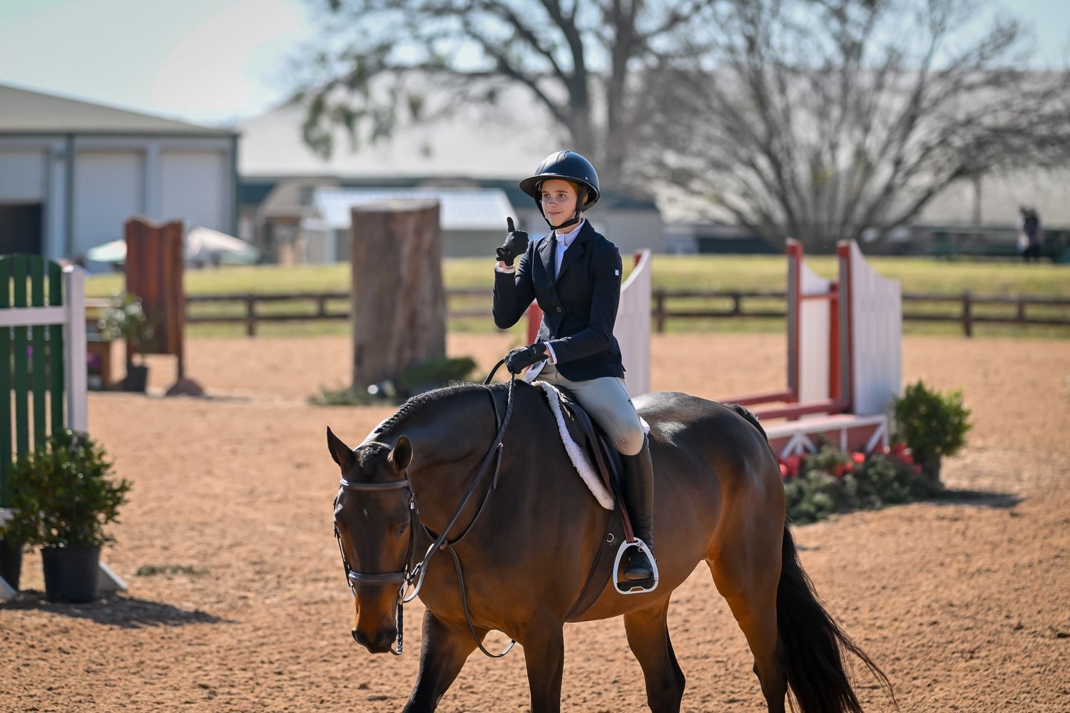 a young equestrian giving a thumbs up to the trainer and family as she exits the ring at Texas Rose Horse Park in Tyler TX.