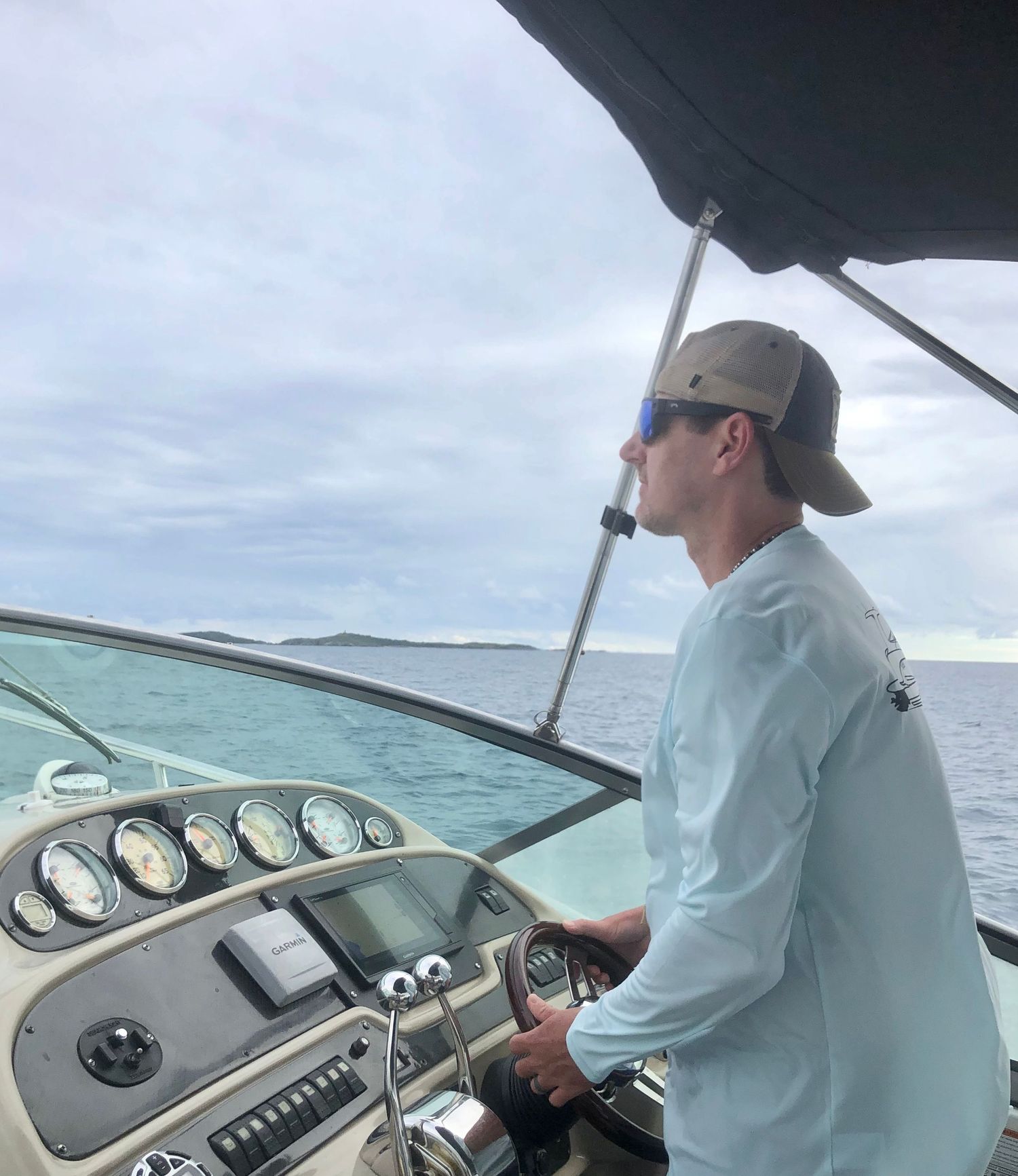 Person in white shirt and cap steering a boat across turquoise waters on a cloudy day.