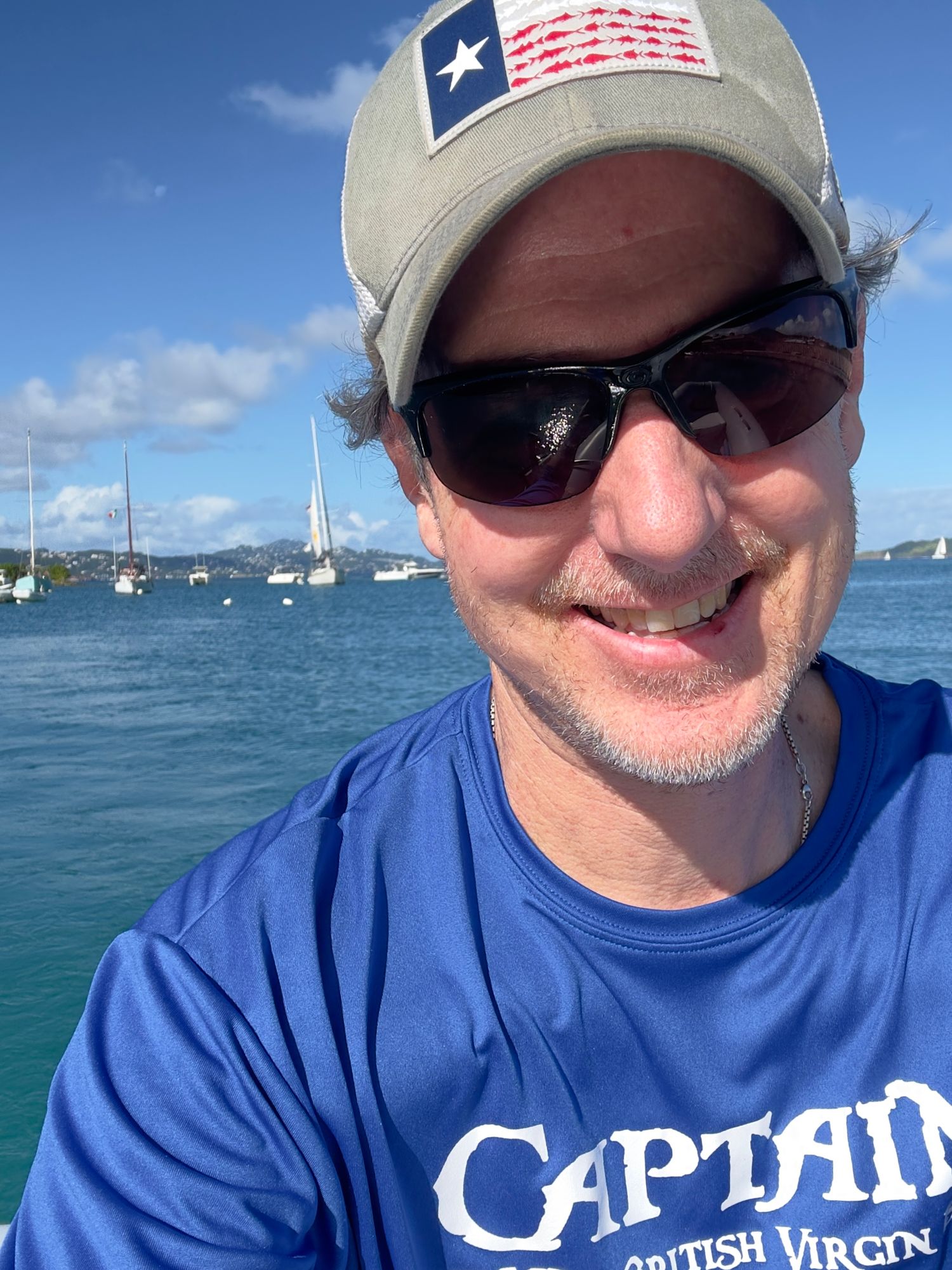 A person in a blue shirt and baseball cap enjoys time on a boat with blue ocean waters in the background.