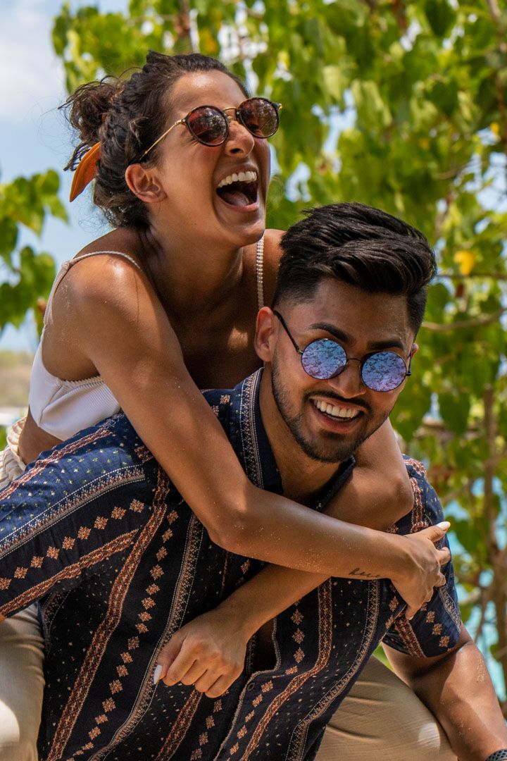 Two people laughing and having fun outdoors on a sunny day, wearing sunglasses and casual summer clothing.