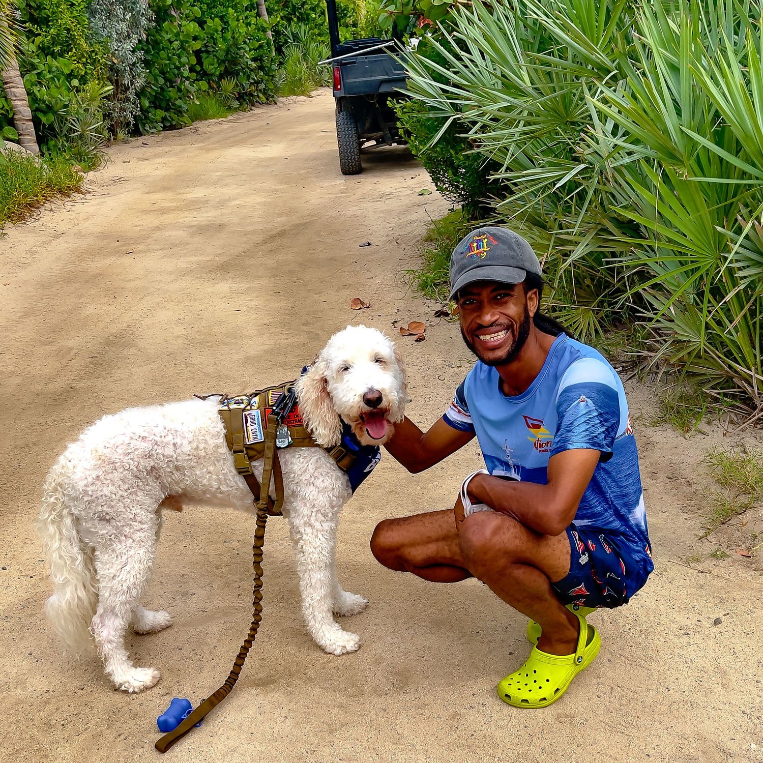 Necker Island tour guide, Gumption, crouches down to pet a fluffy white dog on a sandy path surrounded by palm trees.