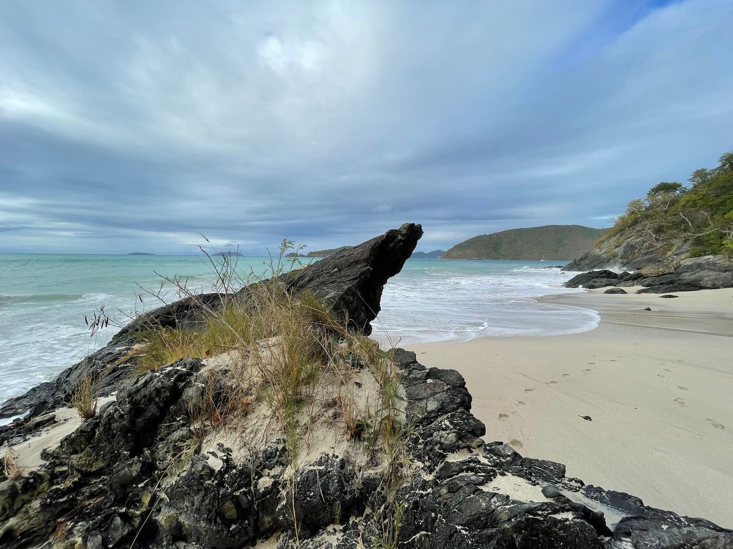 Scenic coastal beach landscape with rugged cliffs, rolling waves, and cloudy skies along a pristine shoreline.