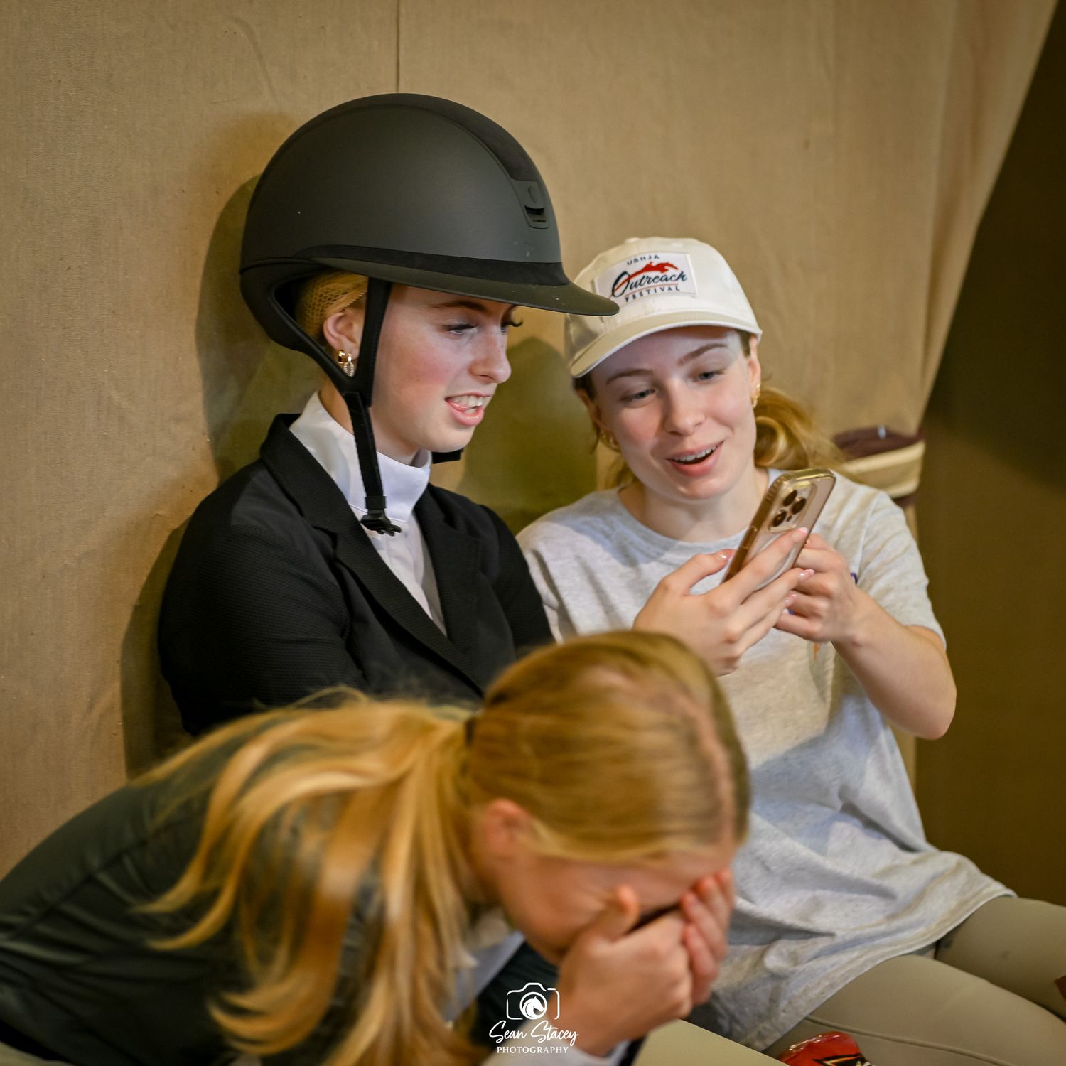 Two riders in equestrian gear reviewing content on a mobile device between training sessions.