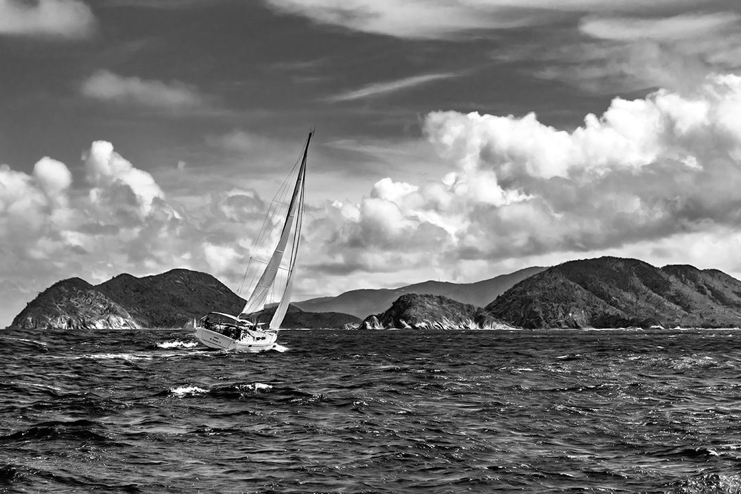 A dramatic black and white landscape photograph showing a heeled sailboat & coastline and stormy ocean waves in the Virgin Islands.