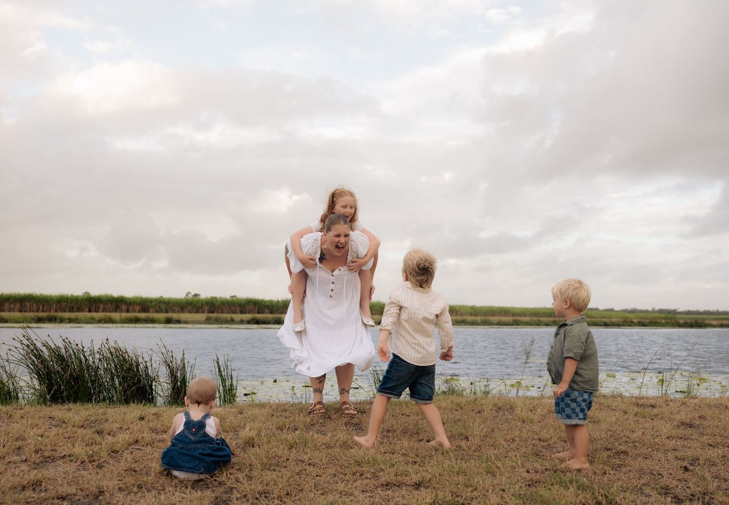 Family enjoying a playful moment on a grassy bank beside a calm lake.