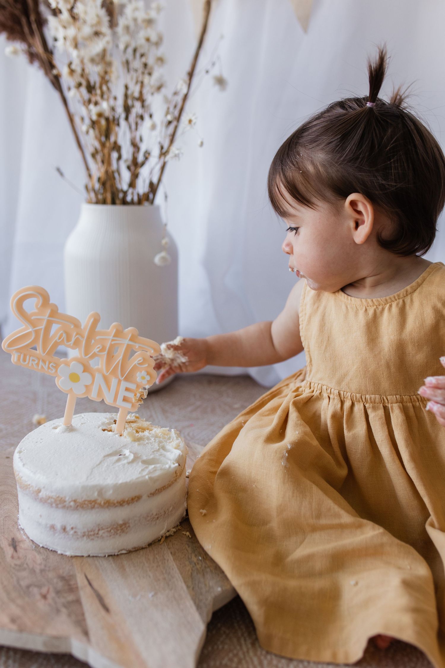 First birthday cake decorating scene with sparkle one topper and mustard dress.
