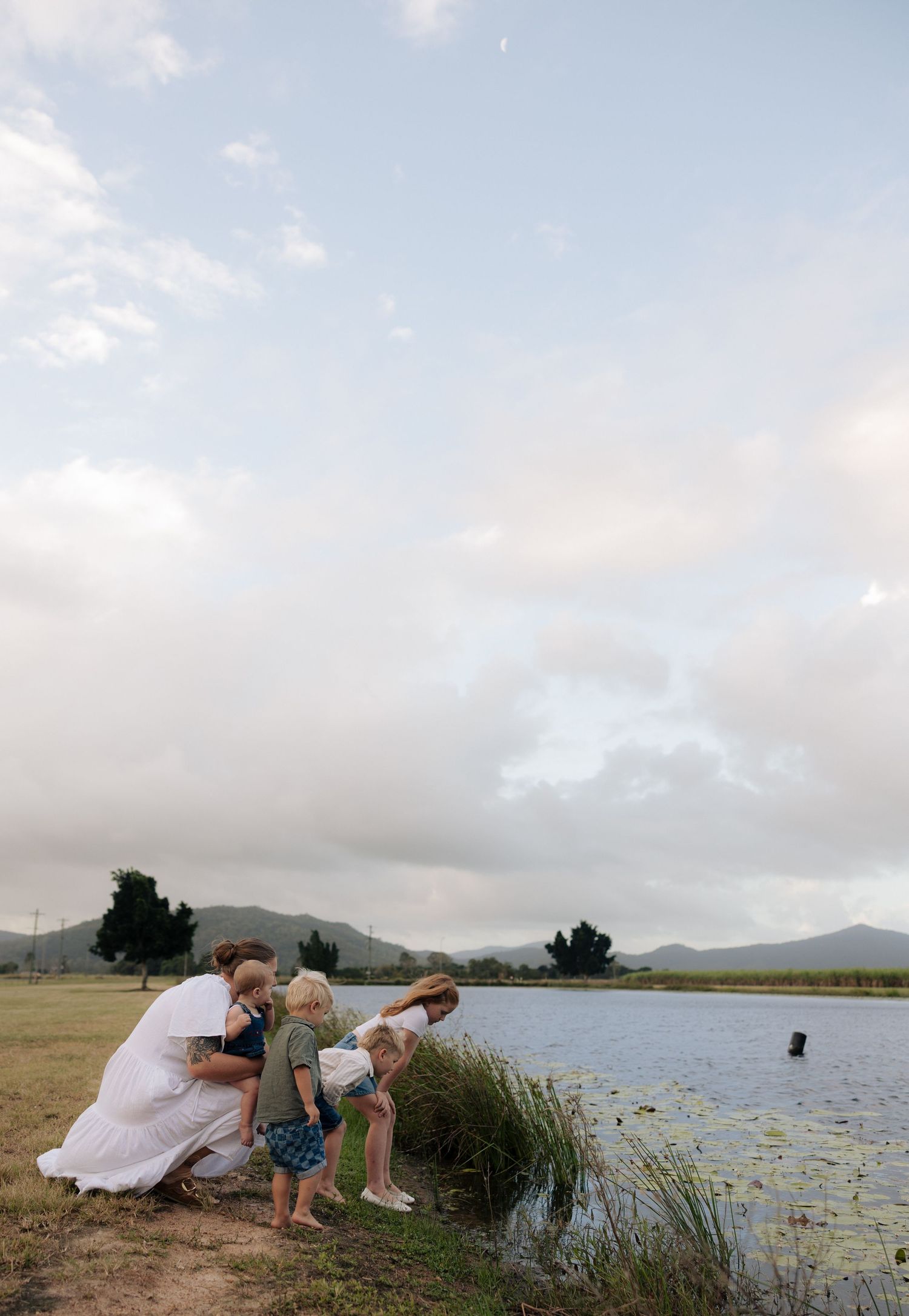 Family enjoying a moment by a serene lake with mountains in the background on a cloudy day.
