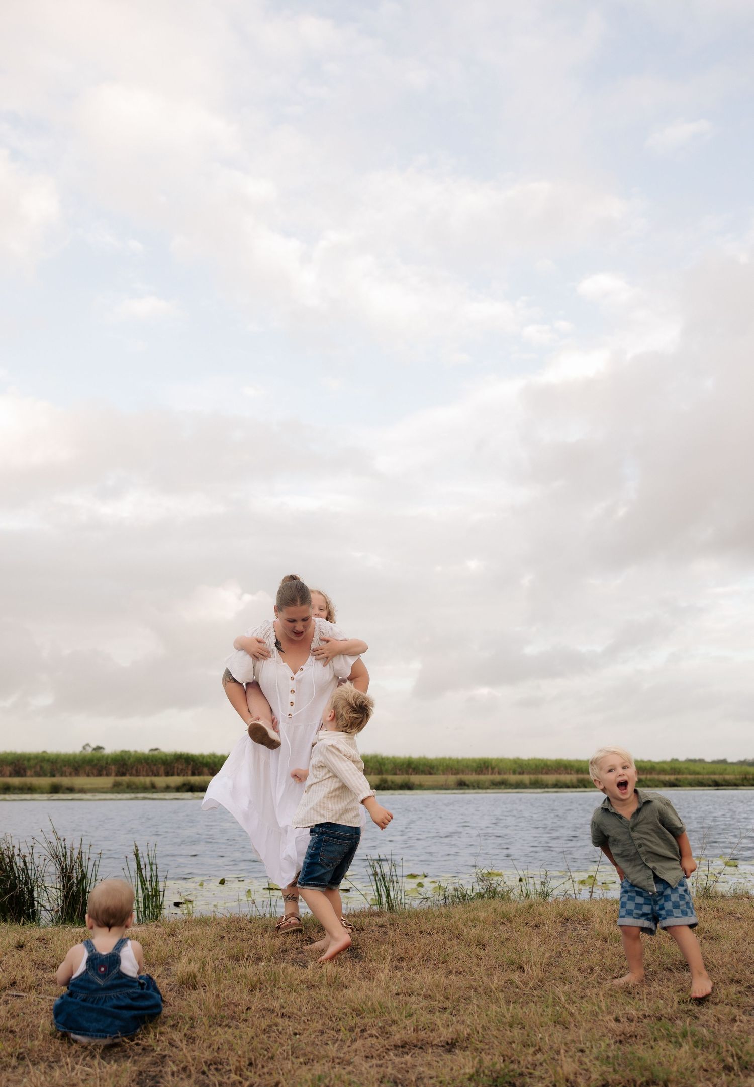 Parent and children playing energetically by a peaceful waterfront.